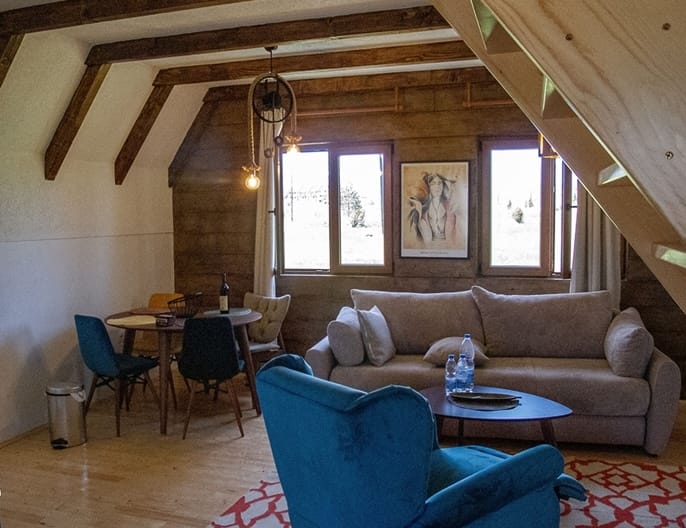 Living room in a wooden house in Žabljak, Montenegro: a soft sofa, a blue armchair, a dining area, and panoramic windows.
