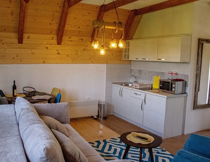 Living room with kitchen area, grey sofa, wooden ceiling, and rope pendant light near dining table.