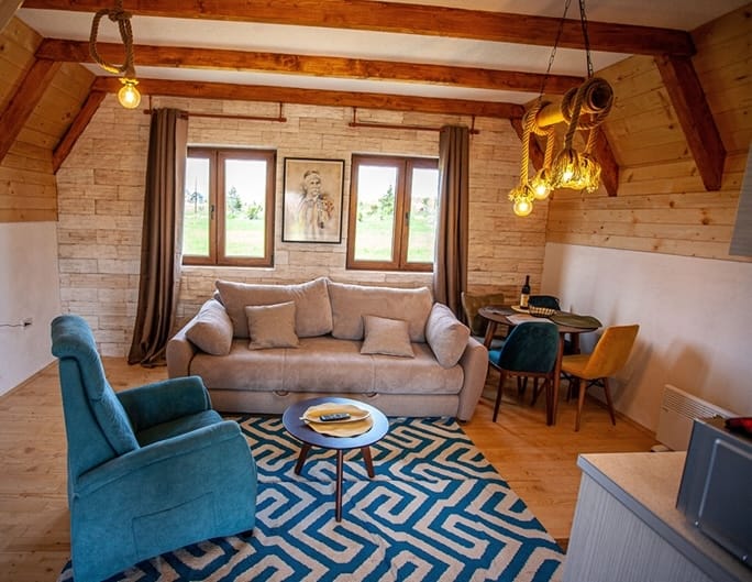 Living room with beige sofa, blue armchair, coffee table, wooden ceiling beams and dining area.