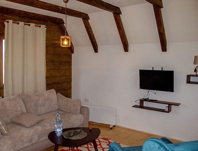 Living room in a house in Žabljak, Montenegro: a soft sofa, wooden ceiling beams, TV, and a stylish interior.
