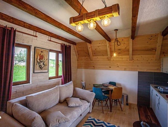 Rustic-style living room with wooden beams in a house, Žabljak, Montenegro: a soft sofa, dining area, and mountain view.