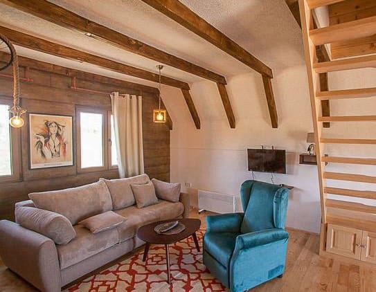 Living room in a wooden style with beams and a staircase in a house, Žabljak, Montenegro: a cozy sofa and a blue armchair.