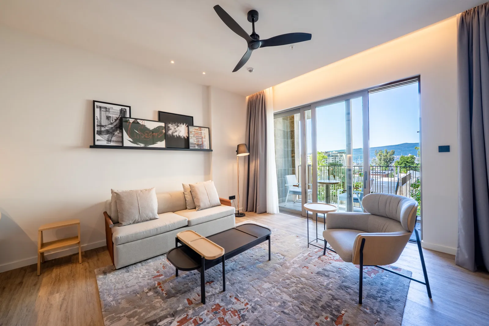 Bright living room with a beige sofa, armchair, coffee table, and ceiling fan next to large sliding glass doors.