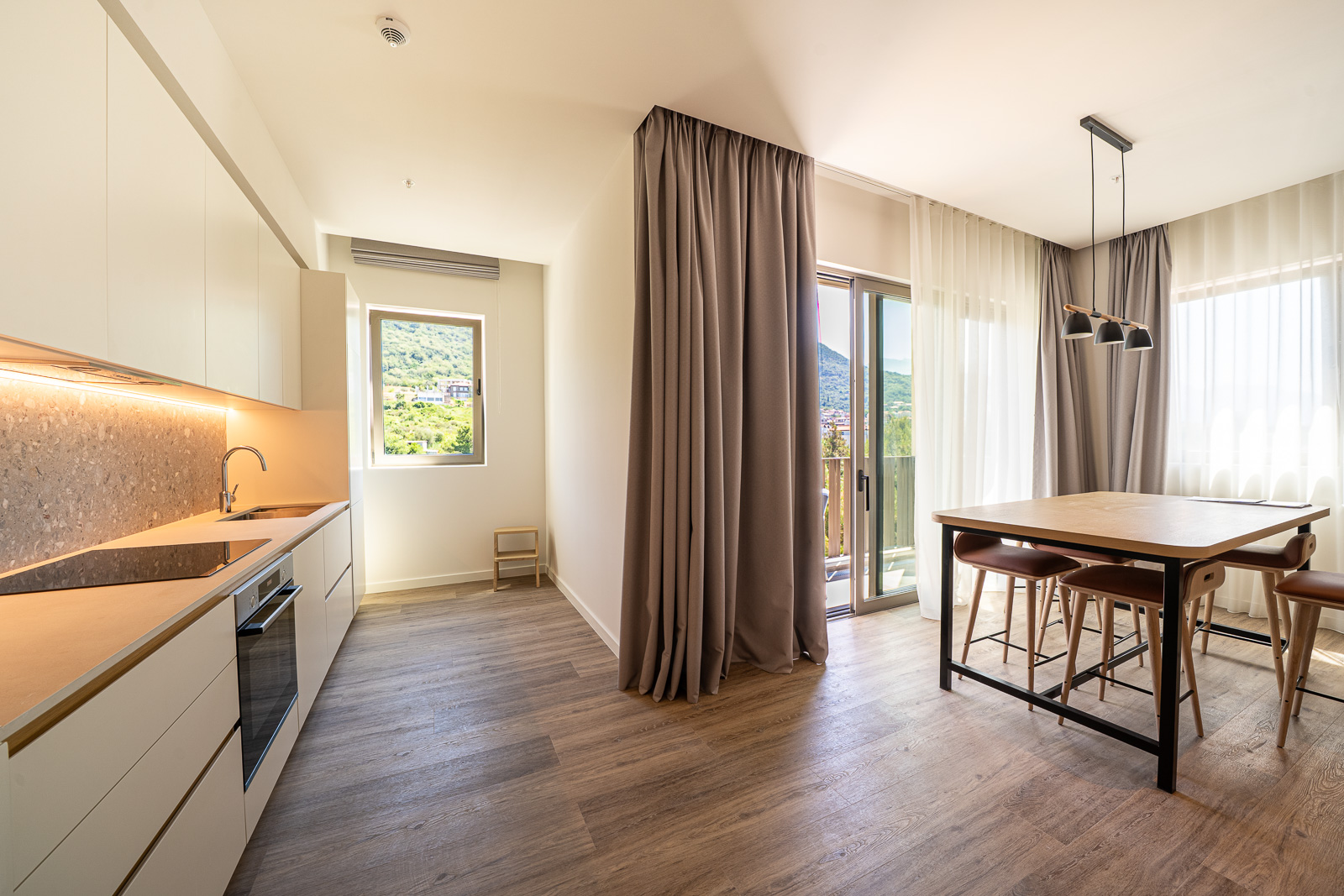 Modern kitchen-dining room in an apartment in Porto Montenegro, Tivat, Montenegro: light-colored cabinetry, view of the mountains and terrace.
