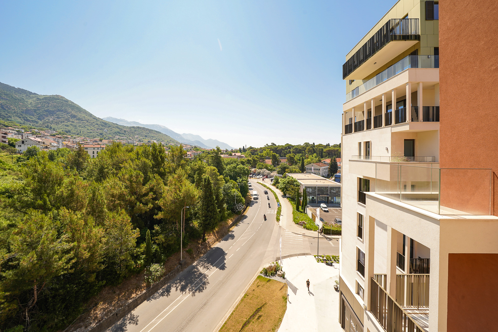 View from the balcony of a modern apartment in Porto Montenegro, Tivat, Montenegro: a panorama of mountains, greenery, and a city road.