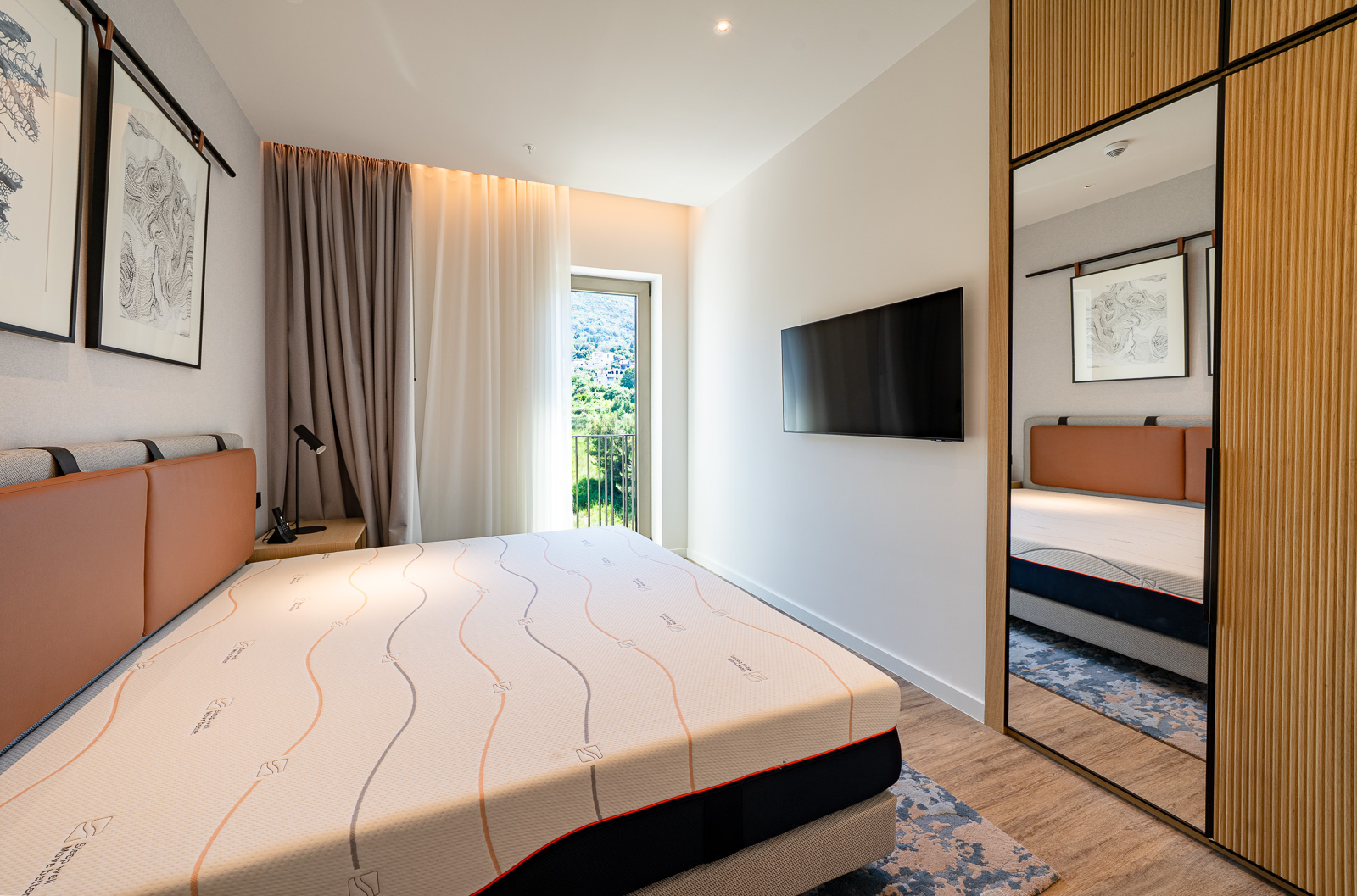 Modern bedroom in Porto Montenegro, Tivat: double bed, mirrored wardrobe, and a view of the mountains of Montenegro.