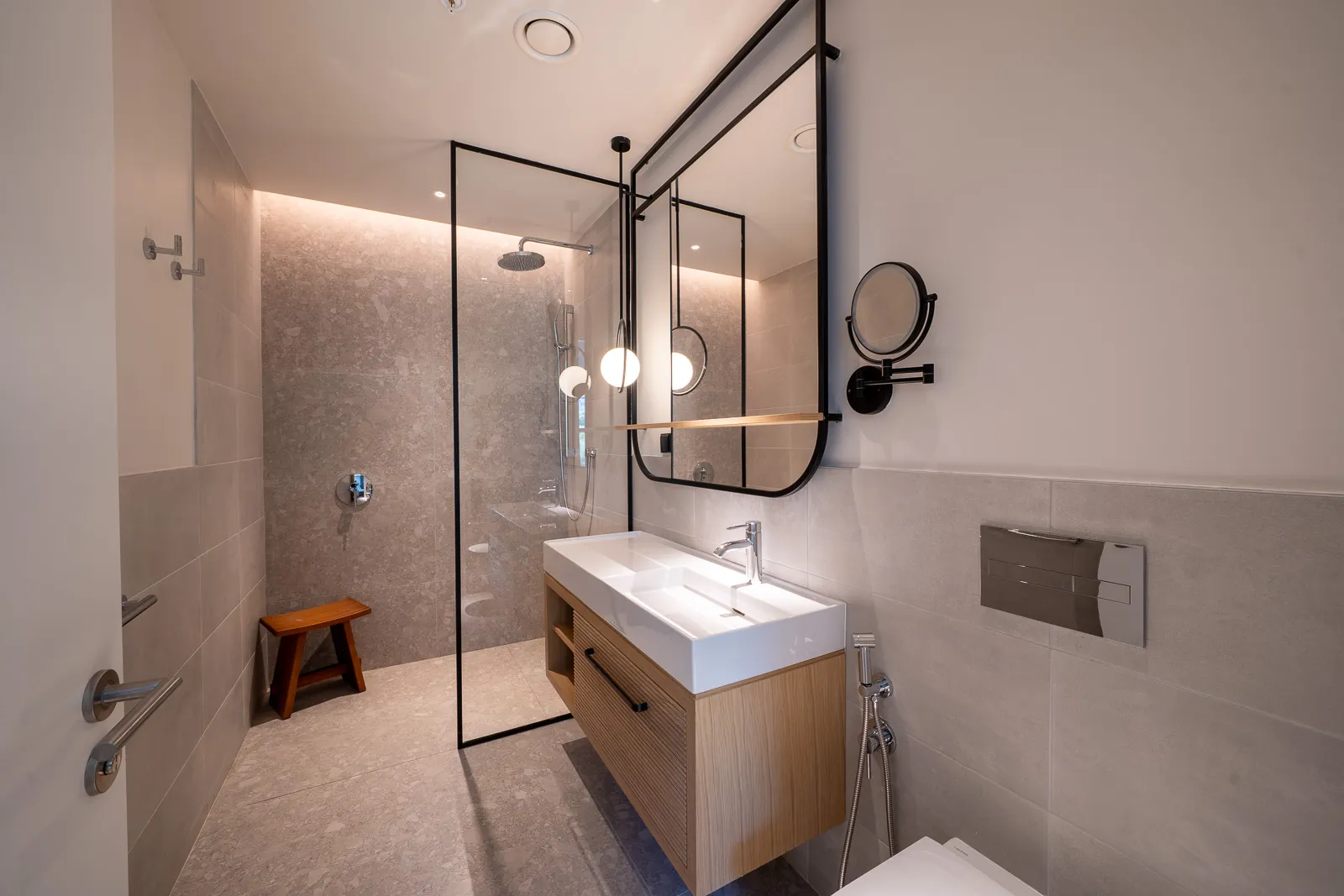 Modern bathroom featuring a glass-enclosed shower, floating wooden vanity with a white sink, and a large black-framed mirror.