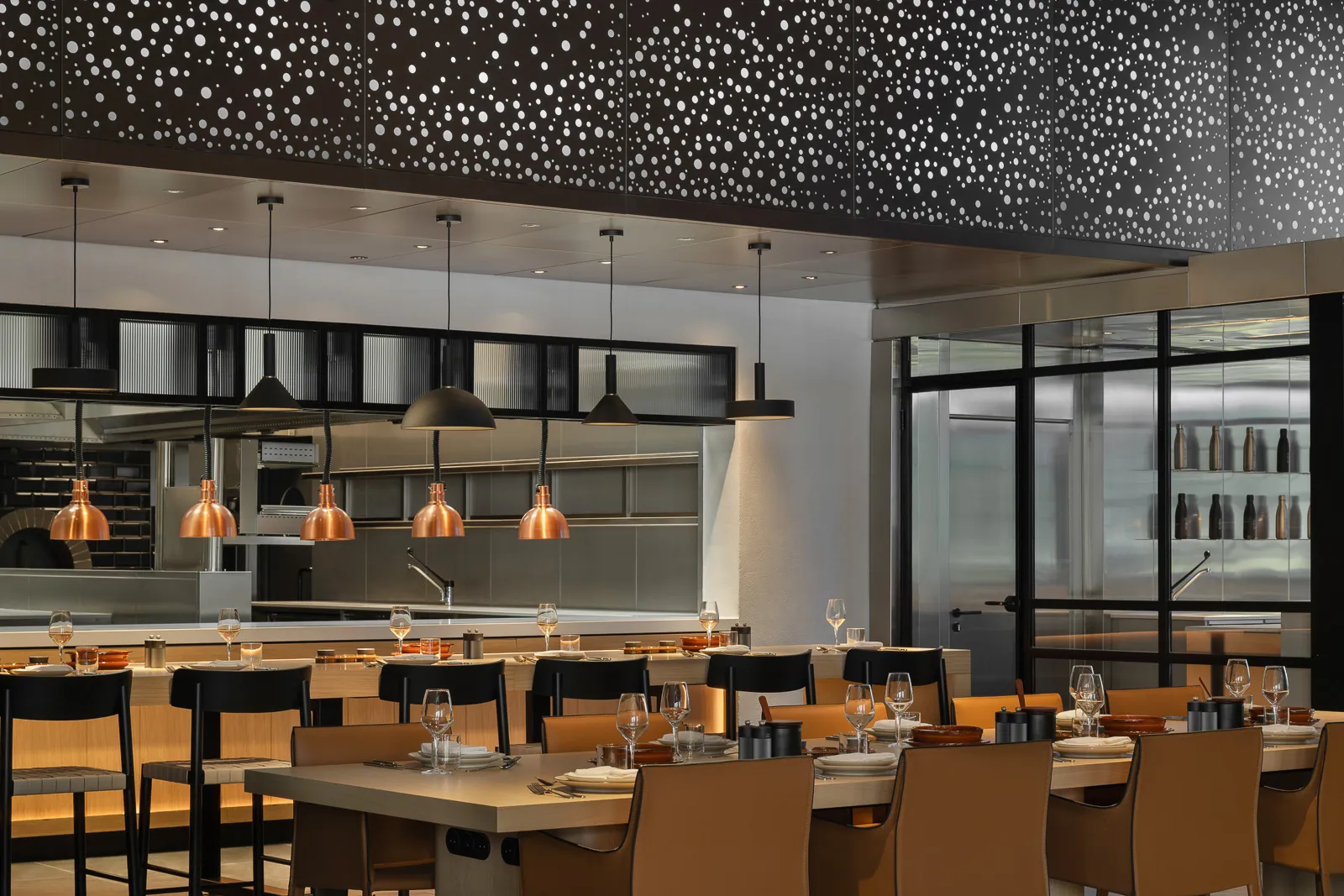 Restaurant interior with set dining tables, a bar counter, and an open kitchen visible in the background.