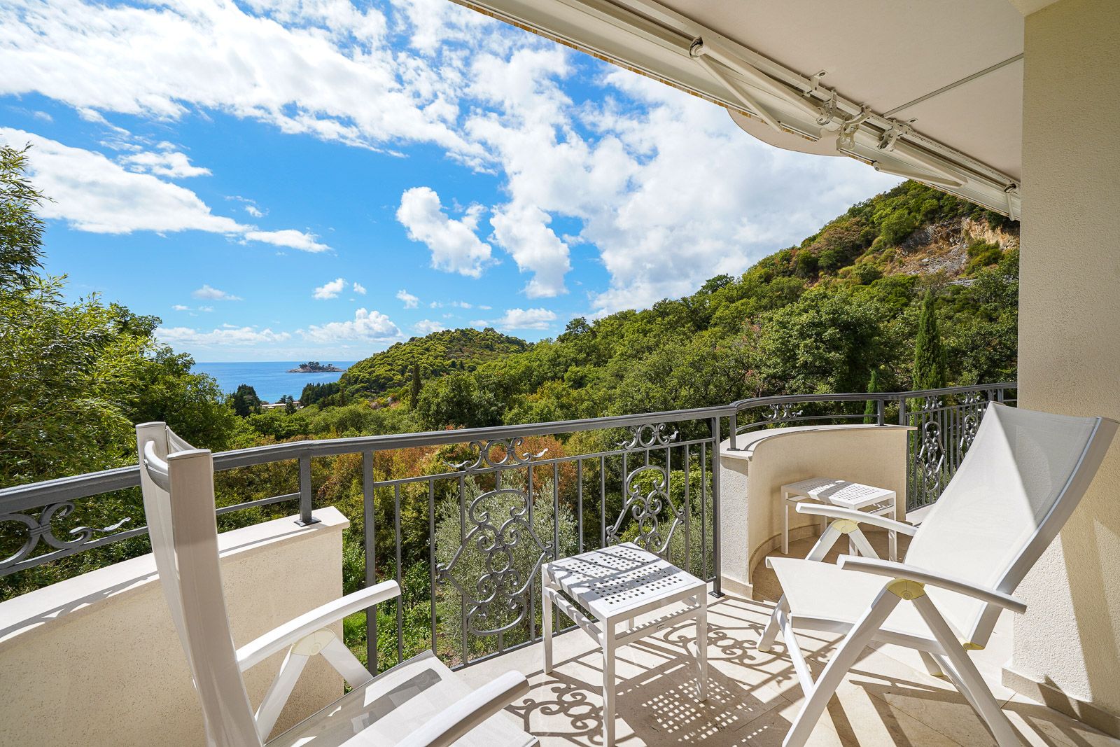 Balcony with sea and mountain views in an apartment in Petrovac, Montenegro: white furniture, wrought-iron railings, and a terrace.
