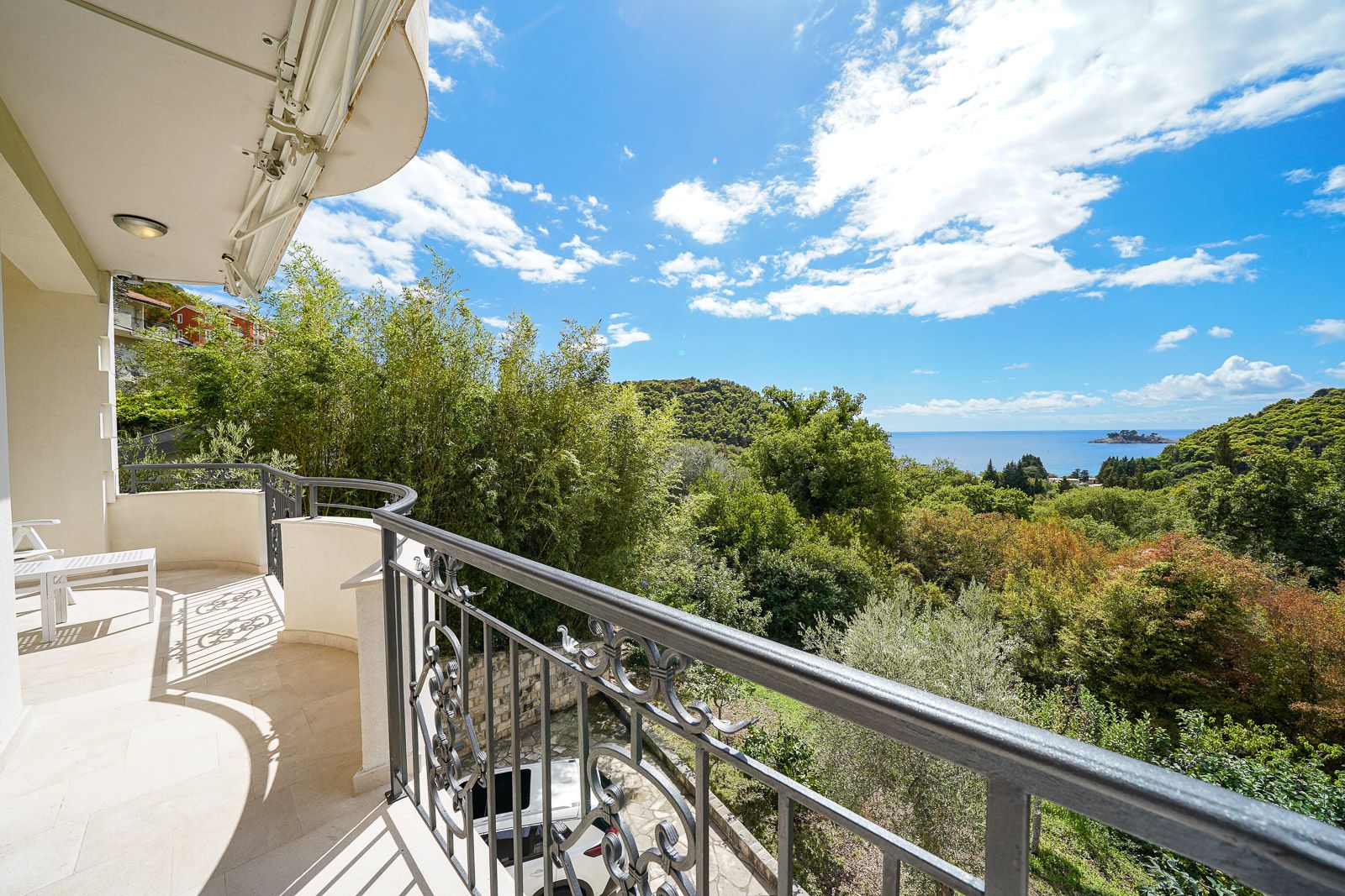 Spacious apartment balcony in Petrovac, Montenegro, with wrought-iron railing and panoramic views of the sea and greenery.