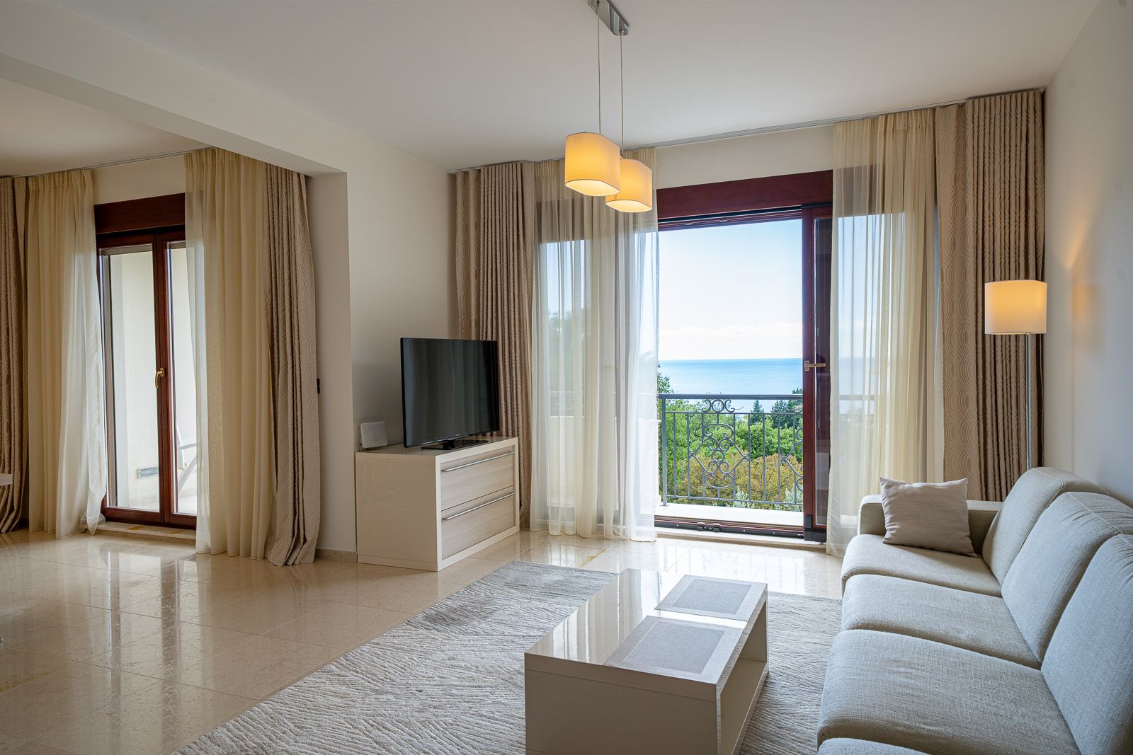 Living room in an apartment in Petrovac, Montenegro: bright interior, sofa, TV area, and panoramic sea view from the balcony.