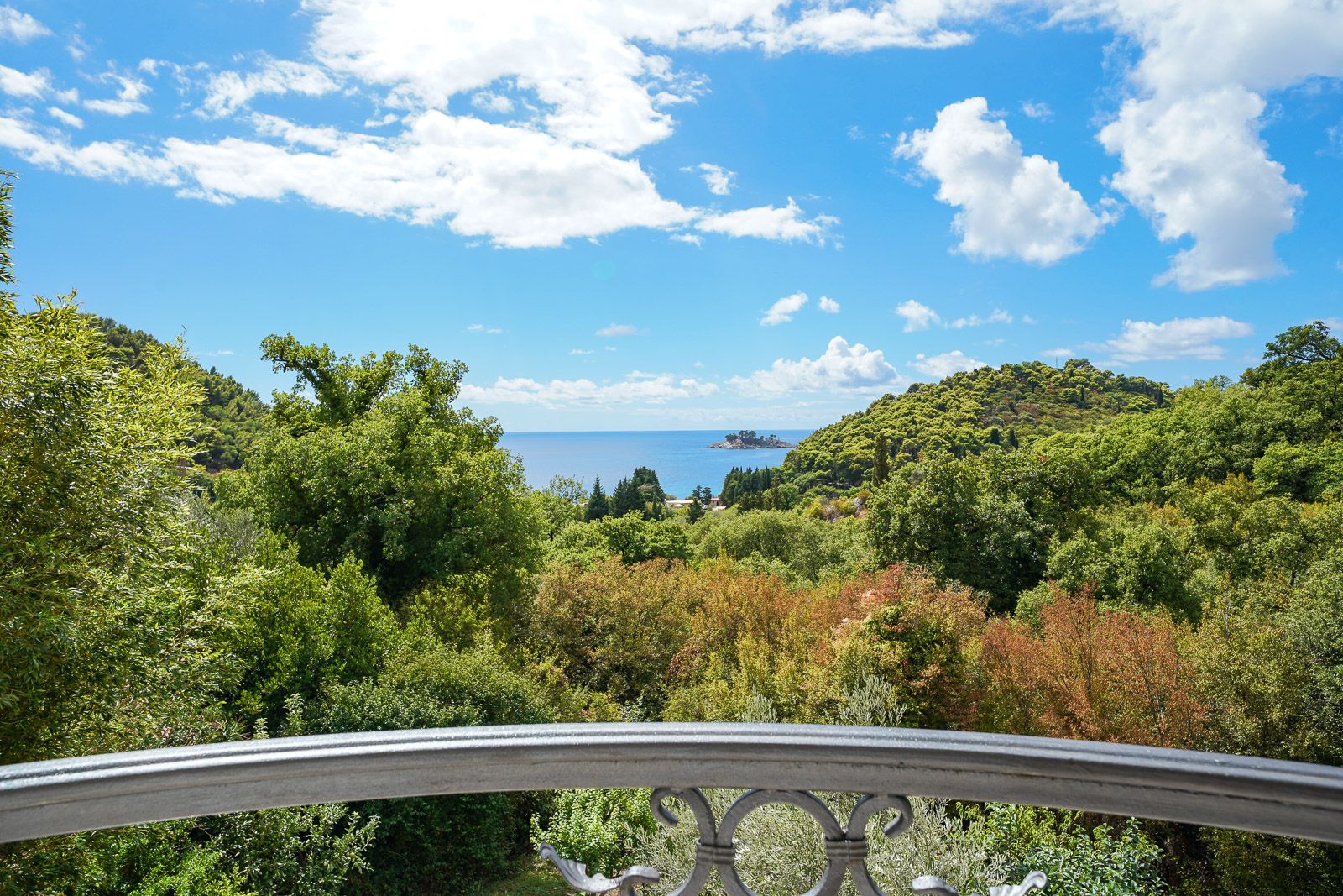 View from the apartment balcony in Petrovac, Montenegro: a panorama of the Adriatic Sea, green forest, and Katic Island.