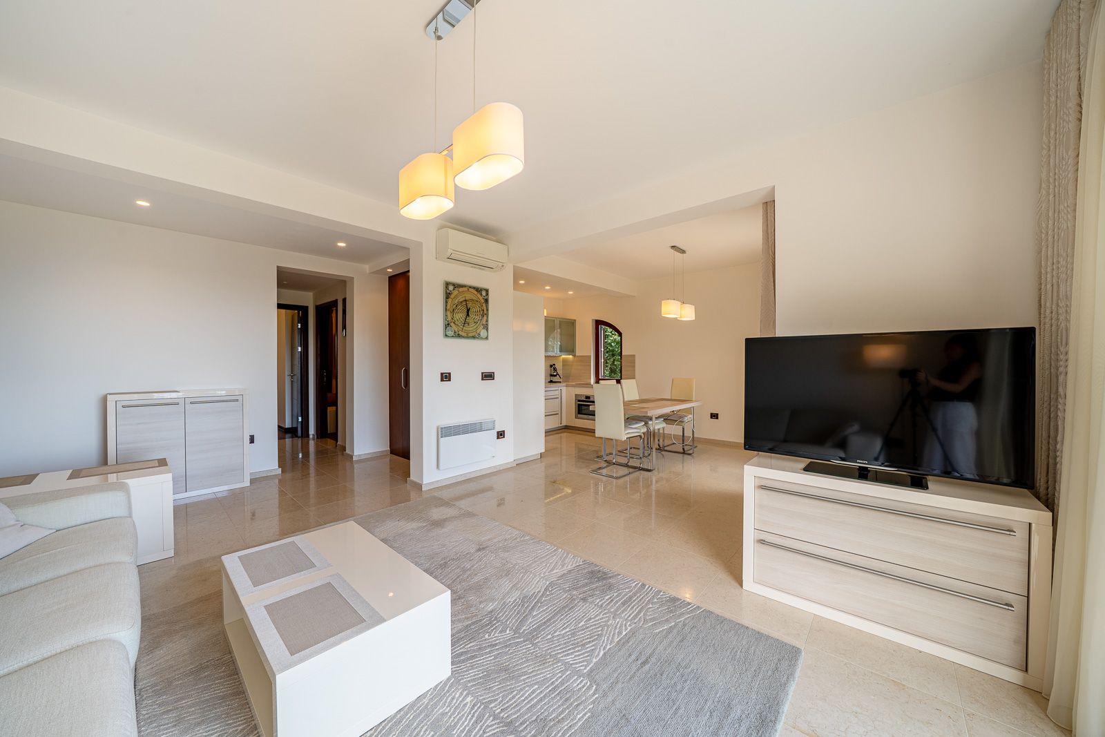 Modern living room with dining area in an apartment in Petrovac, Montenegro: light furniture, TV, and tiled floor.