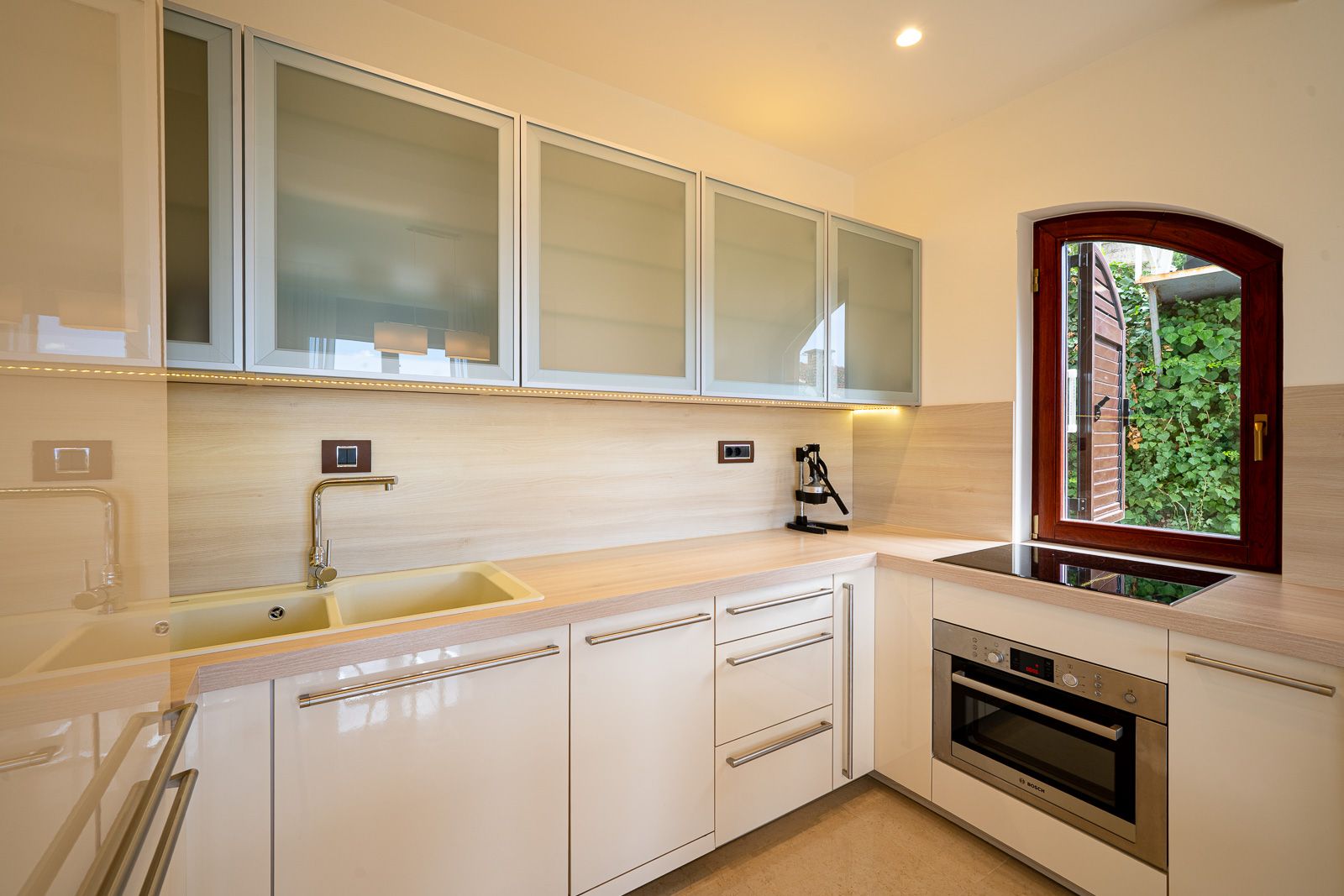 Modern bright kitchen in an apartment in Petrovac, Montenegro: built-in Bosch appliances, matte fronts, and a view of the garden.