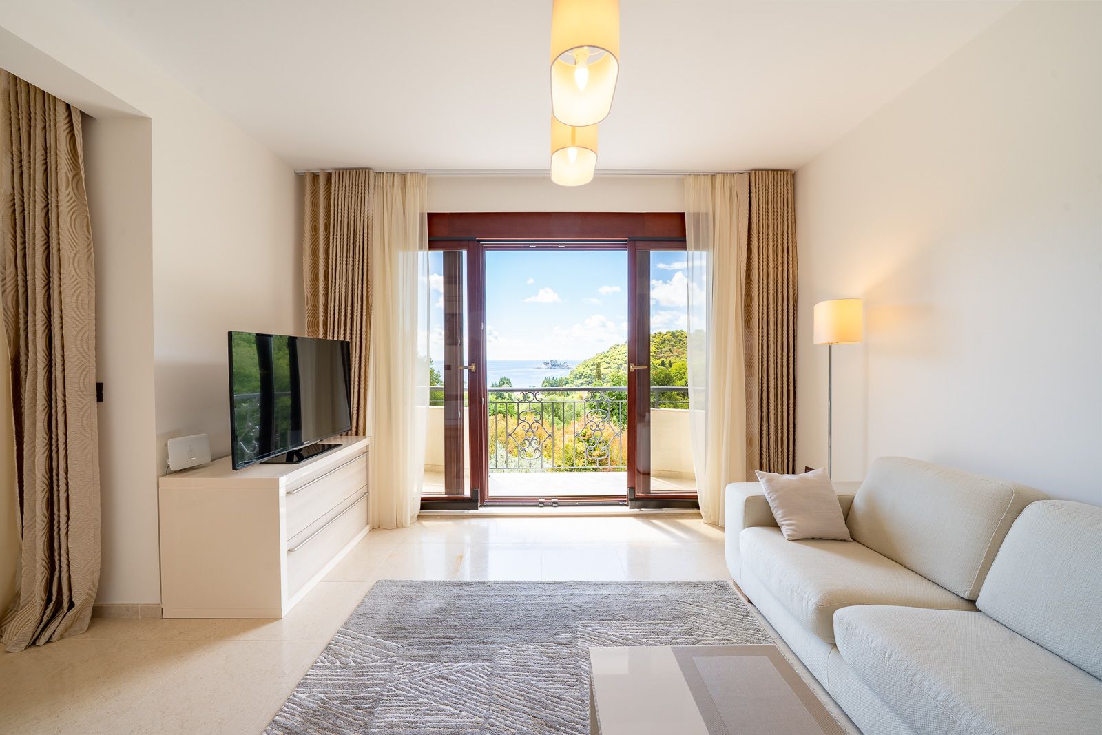 Bright living room in an apartment in Petrovac, Montenegro: modern furniture, TV area, and panoramic sea view from the balcony.