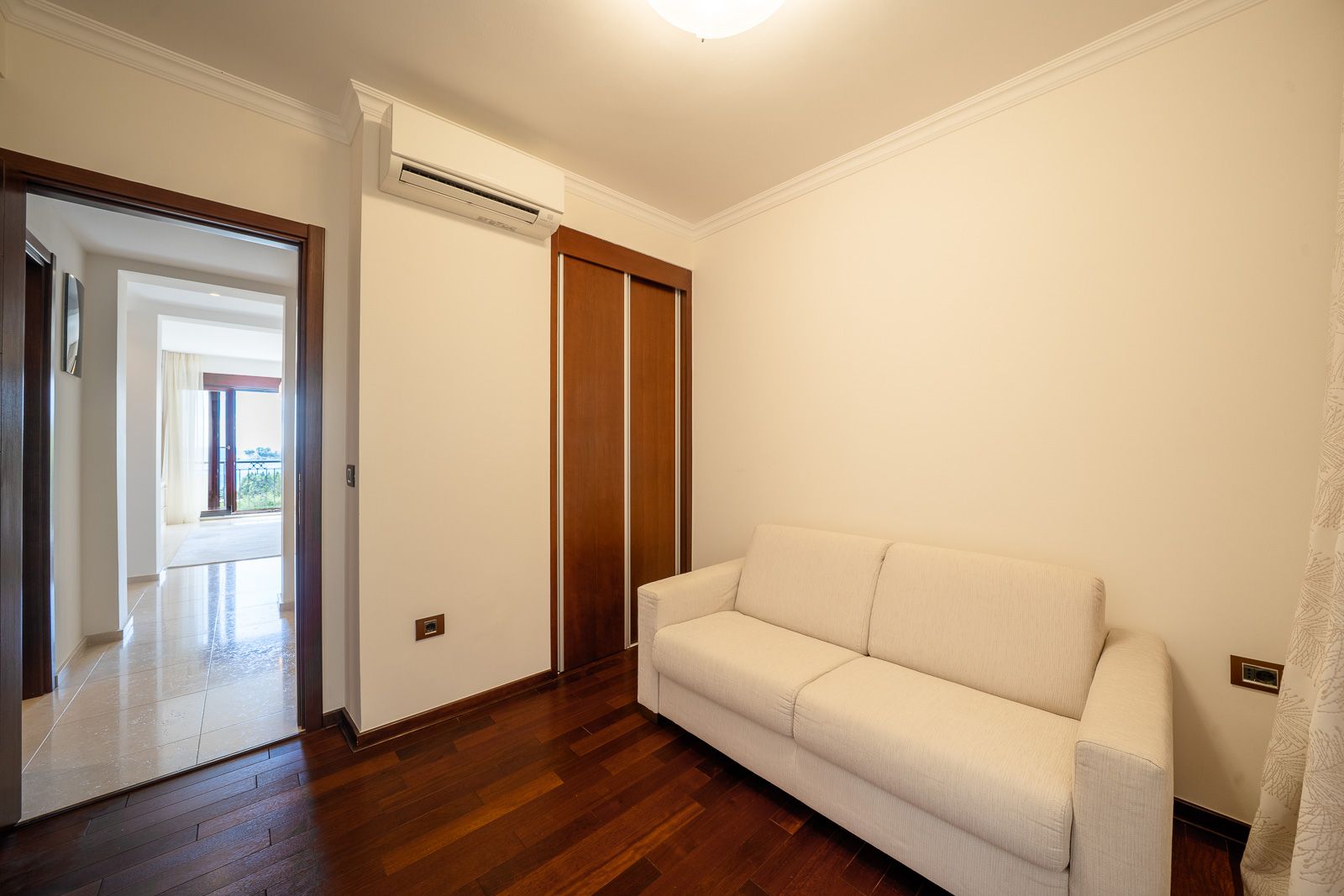 Bright living room with a white sofa and wooden cabinet in an apartment in Petrovac, Montenegro, with a view of the terrace.