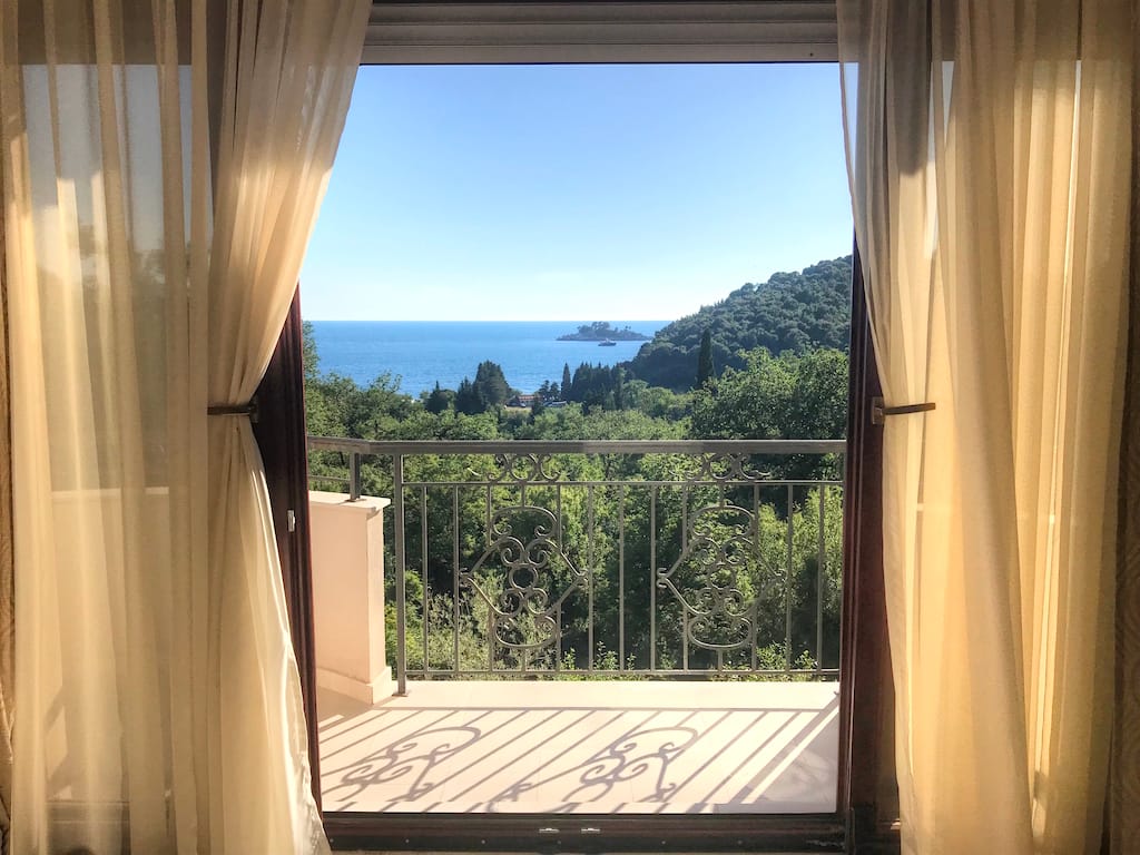 View from the apartment balcony in Petrovac, Montenegro: a panorama of the sea, islands, and greenery through a wrought-iron railing.