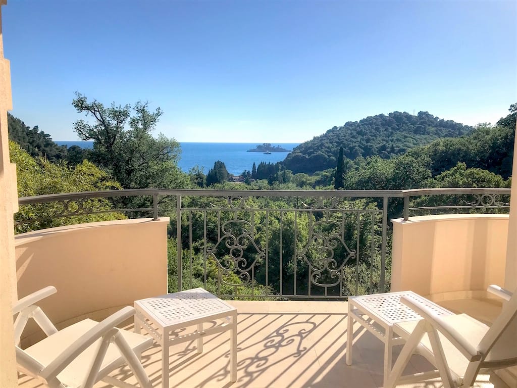 Balcony with wrought-iron railing and furniture in an apartment in Petrovac, Montenegro, with panoramic views of the sea and greenery.