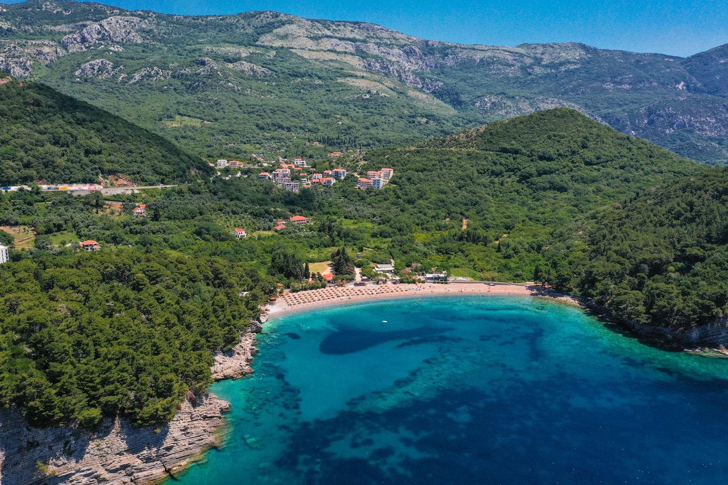 Panoramic view of Lucice Beach and green mountains in Petrovac, Montenegro: a picturesque bay with azure water and forest.