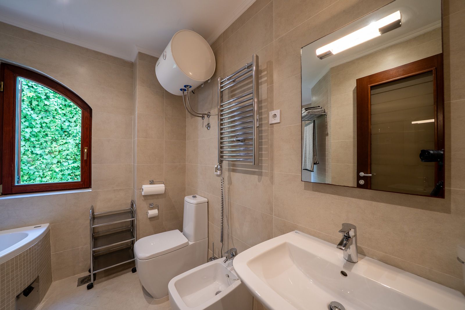 Modern bathroom in an apartment in Petrovac, Montenegro: white sanitary ware, bidet, mirror, and a window overlooking greenery.
