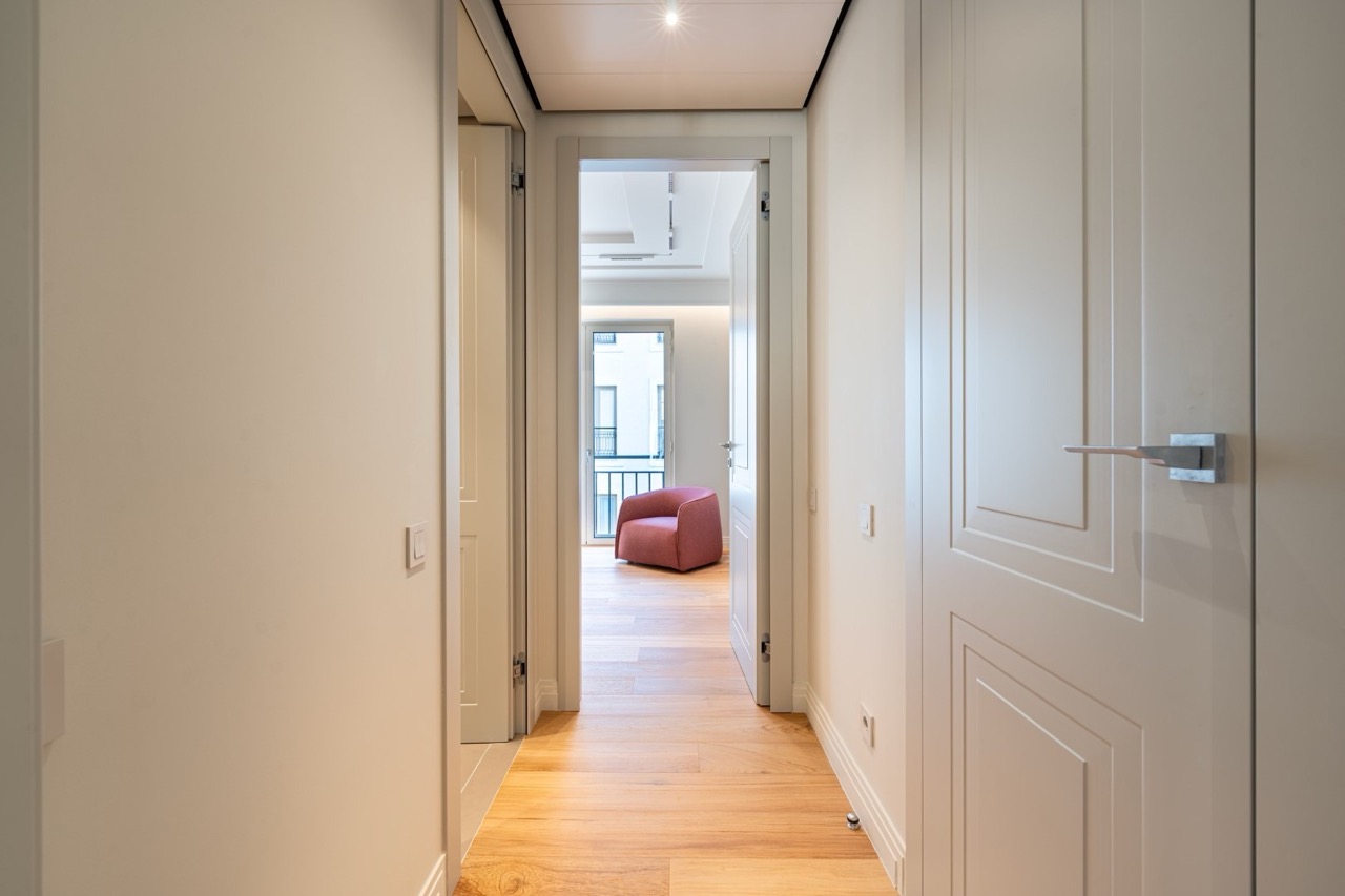 Bright hallway in an apartment in Porto Montenegro, Tivat, Montenegro: parquet floor, white doors, and a view of a pink armchair.