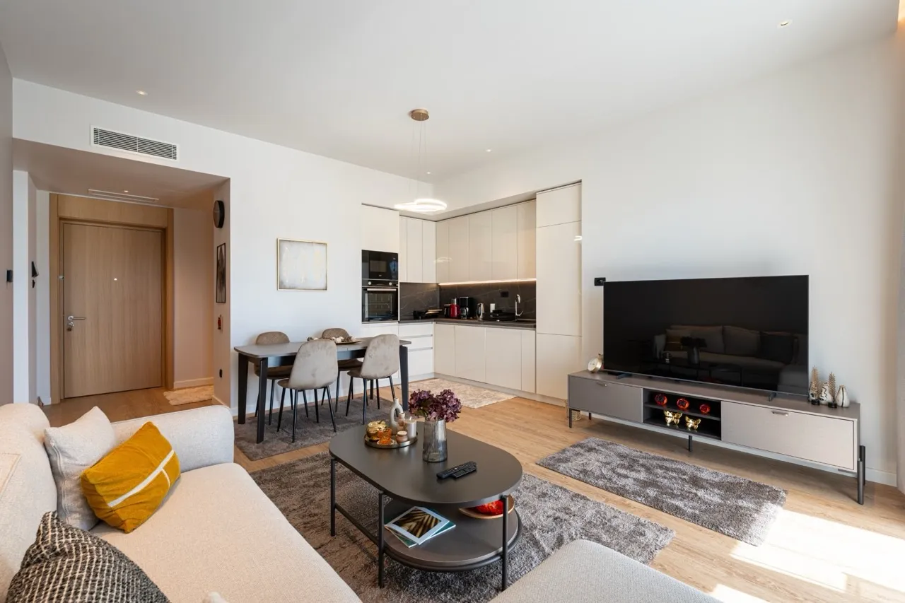 Modern living room featuring a sofa, large TV, and open-plan kitchen area.
