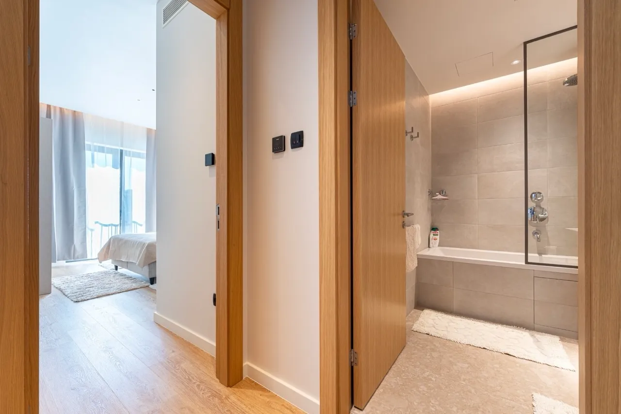 Hallway view showing a bathroom with a shower and a bedroom in the background.