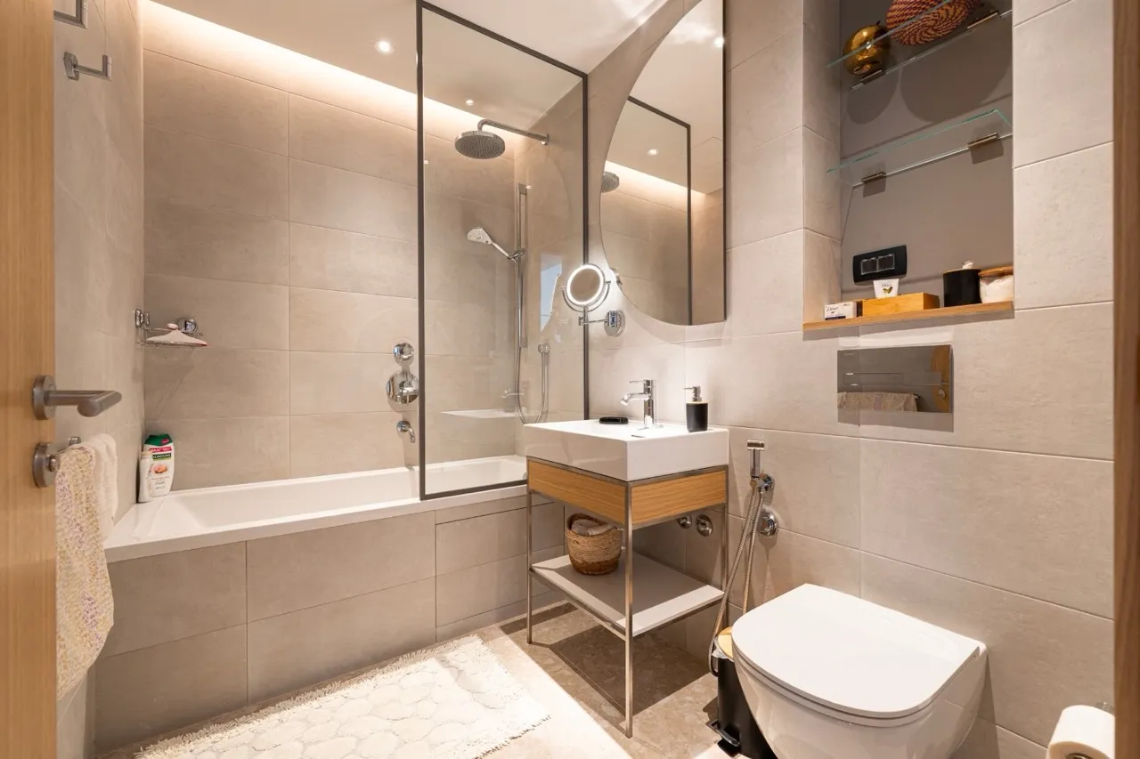 Modern bathroom featuring a shower, vanity sink, toilet, and beige tiled walls.
