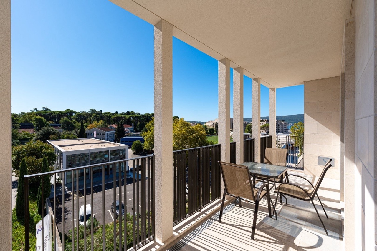 Spacious balcony with garden furniture in Porto Montenegro apartments, Tivat, Montenegro, overlooking the city and greenery.