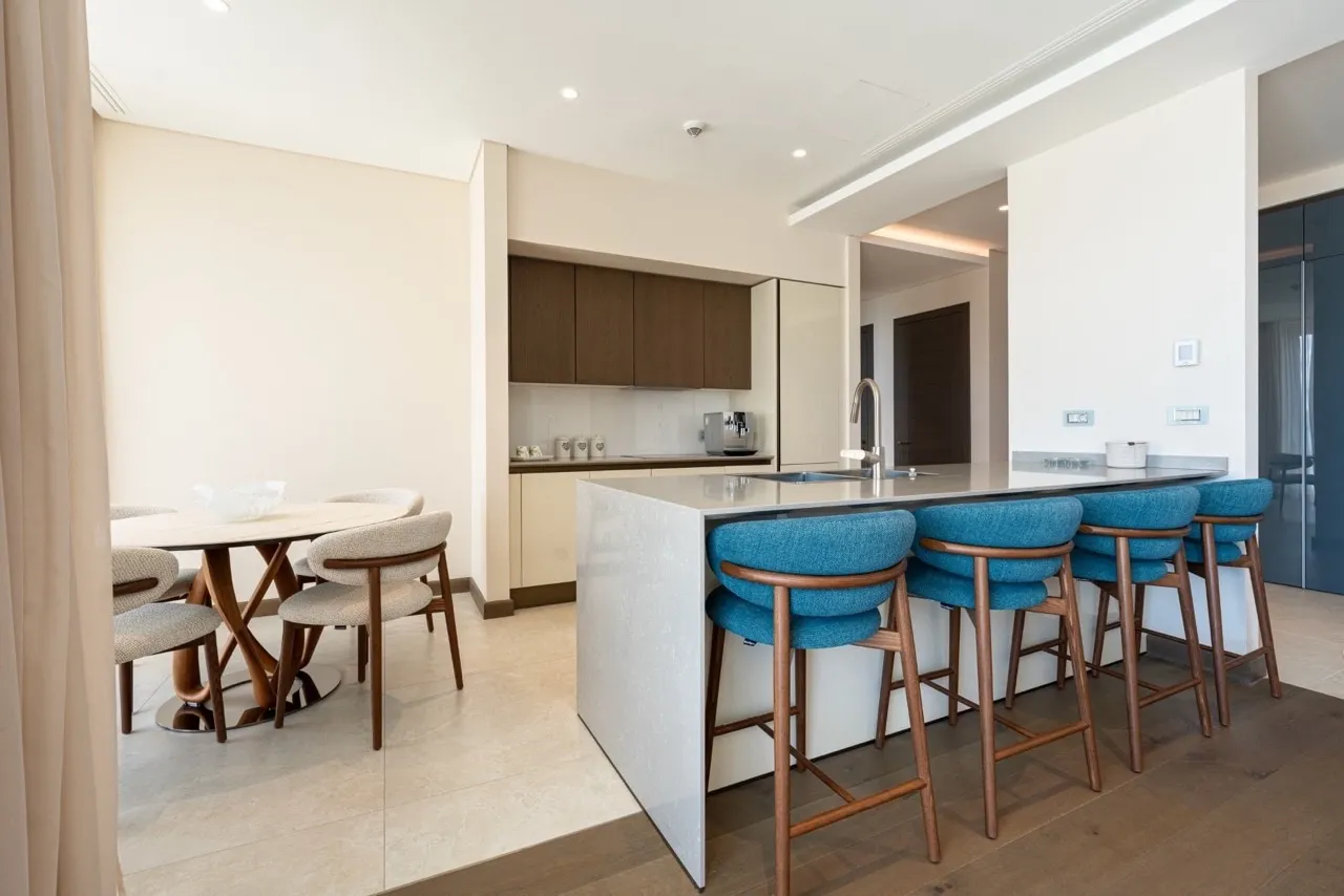 Modern kitchen featuring a central island with blue bar stools and an adjacent dining area with a light table.
