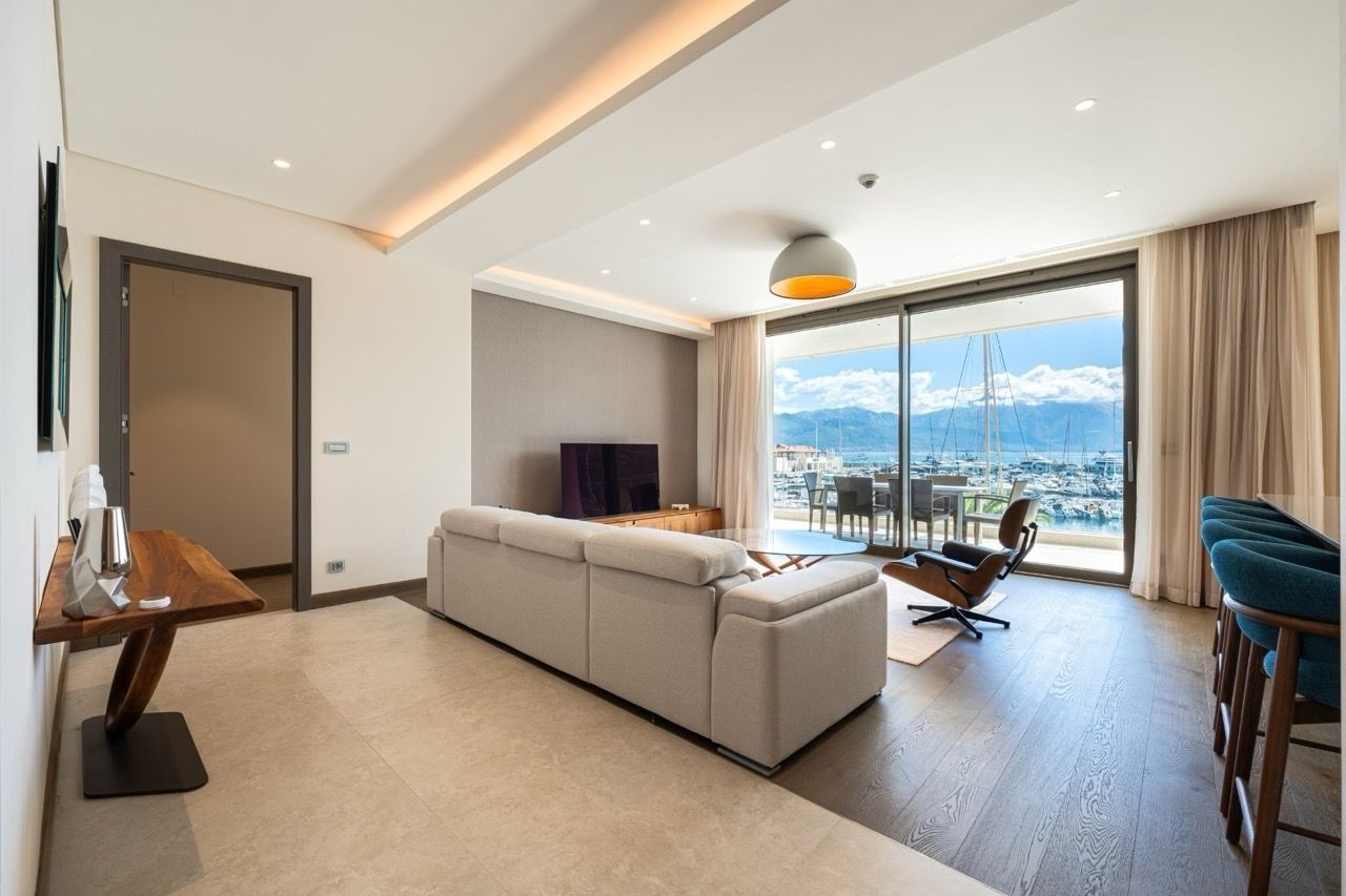 Modern living room in Portonovi, Kumbor, Montenegro: light sofa, panoramic view of the marina and yachts, stylish interior.