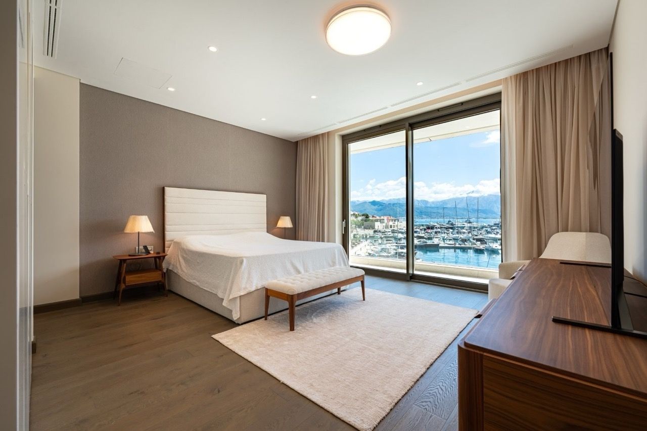 Modern bedroom featuring a double bed, wooden flooring, and a large sliding glass door overlooking a marina.