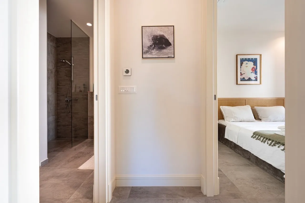 Hallway view showing a bedroom with a bed and a bathroom with a glass shower.