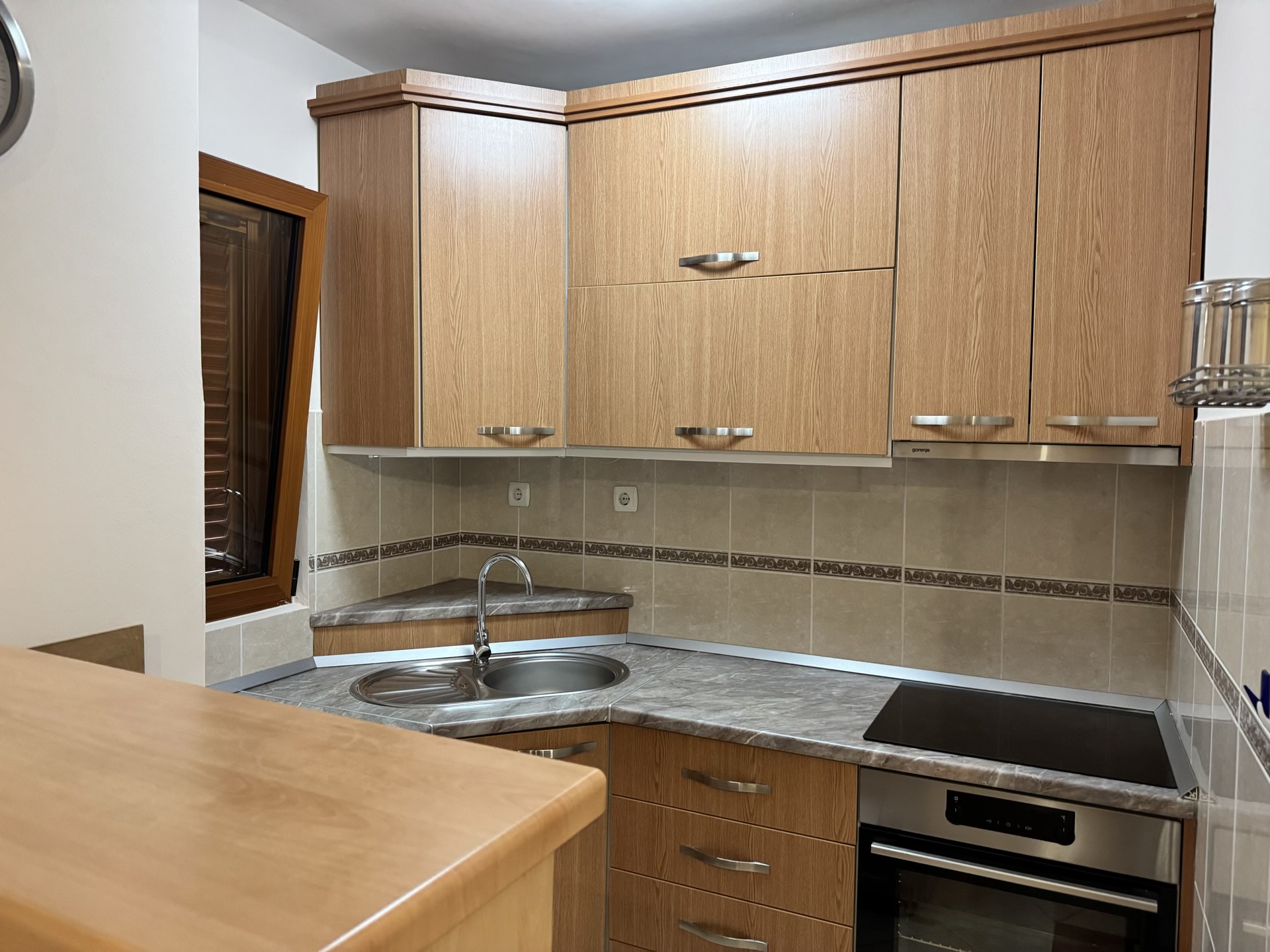 Corner kitchen in an apartment in Budva, Montenegro: wooden fronts, built-in cooktop, sink, and marble-look countertop.
