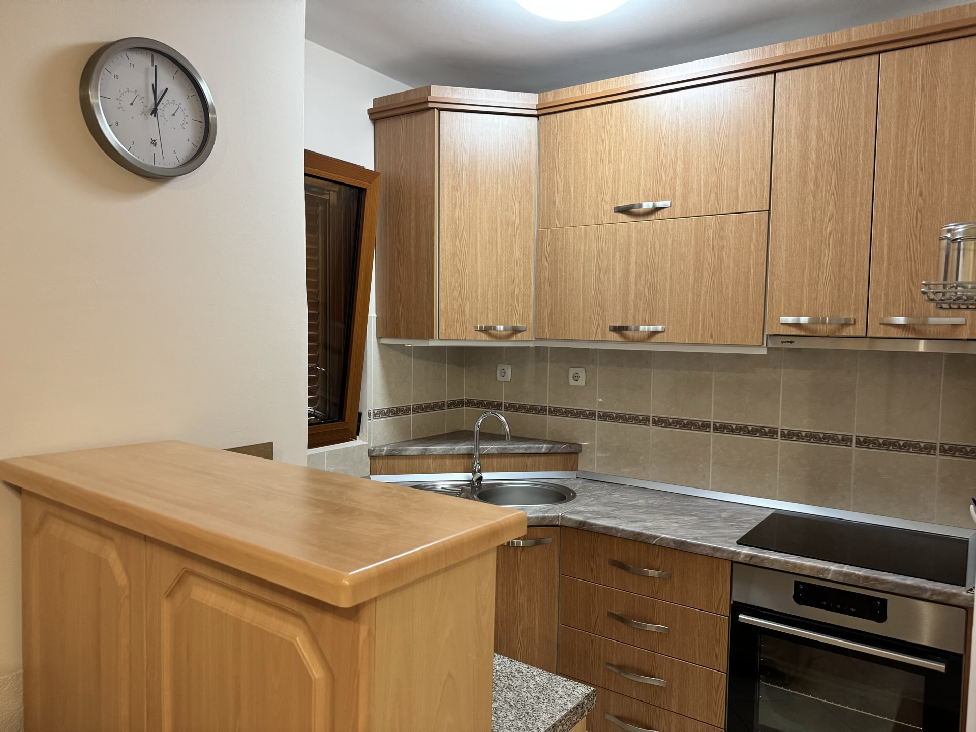 Corner kitchen with wooden fronts and a breakfast bar in an apartment, Budva, Montenegro. Built-in appliances and tile.