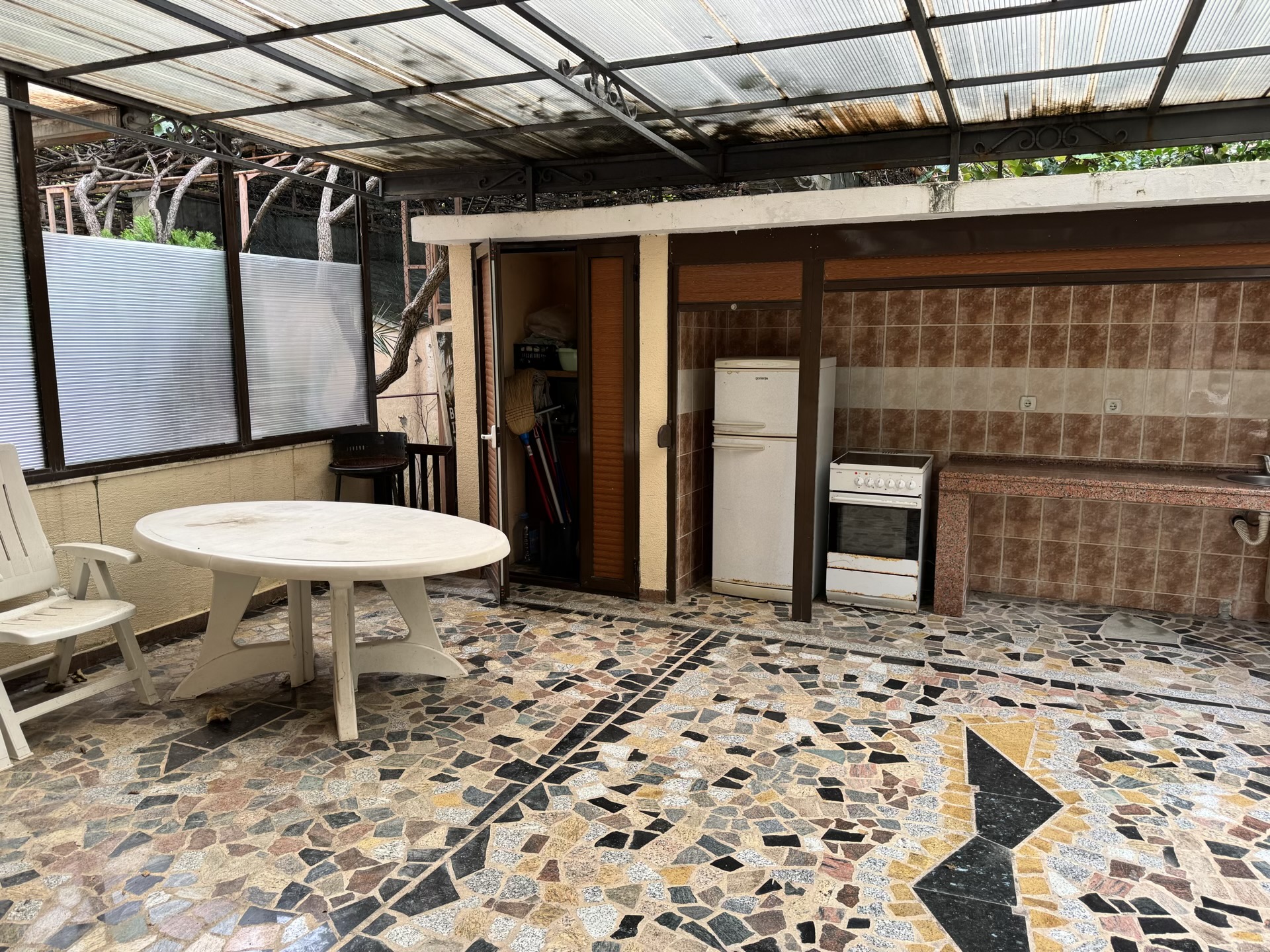 Summer kitchen on the terrace with a stove, refrigerator, and dining area in an apartment, Budva, Montenegro.