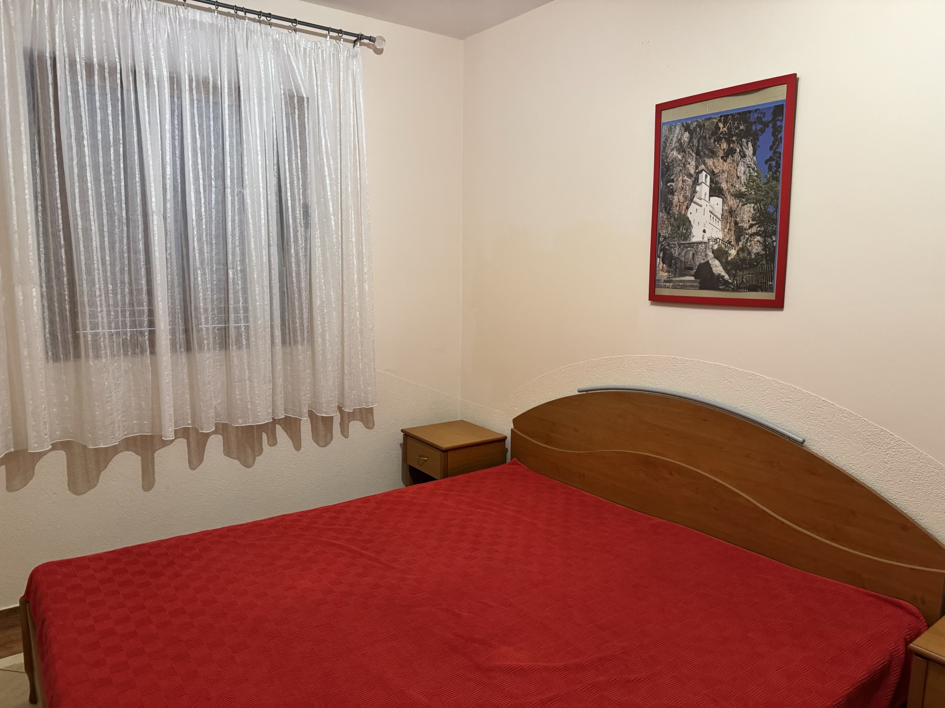 Bedroom in an apartment in Budva, Montenegro: a double bed with a wooden headboard, bedside tables, and a painting on the wall.