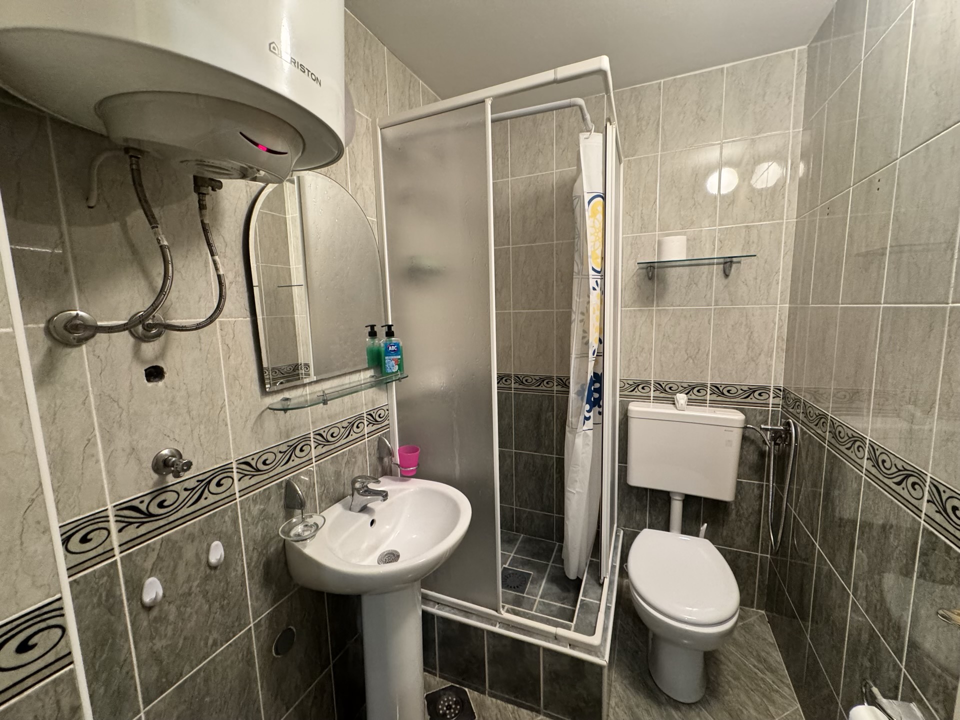 Bathroom in an apartment in Budva, Montenegro: shower cabin, sink, toilet, and an Ariston boiler on the wall.