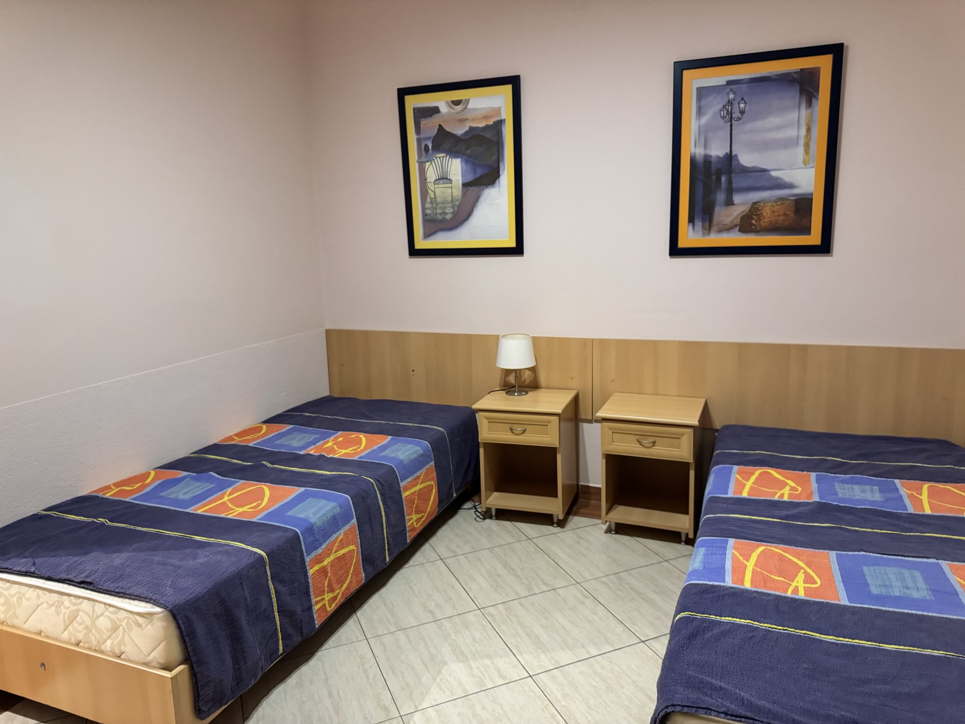 Bedroom with two single beds and bedside tables in an apartment in Budva, Montenegro. Interior with paintings on the walls.