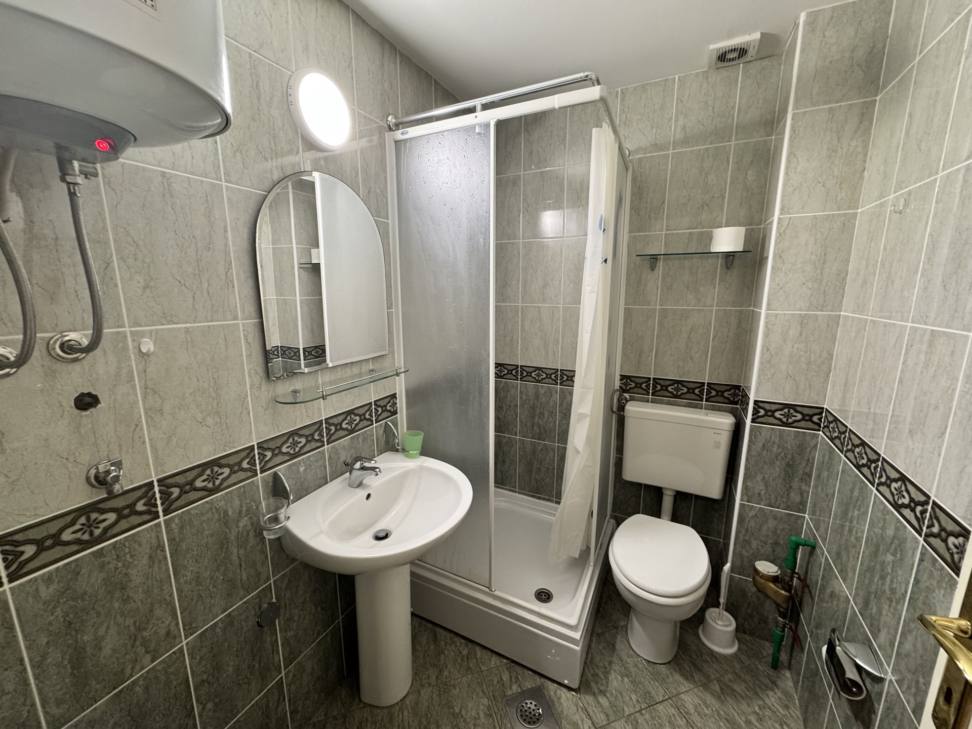 Bathroom in an apartment in Budva, Montenegro: shower cabin, sink, toilet, and gray tile finish.