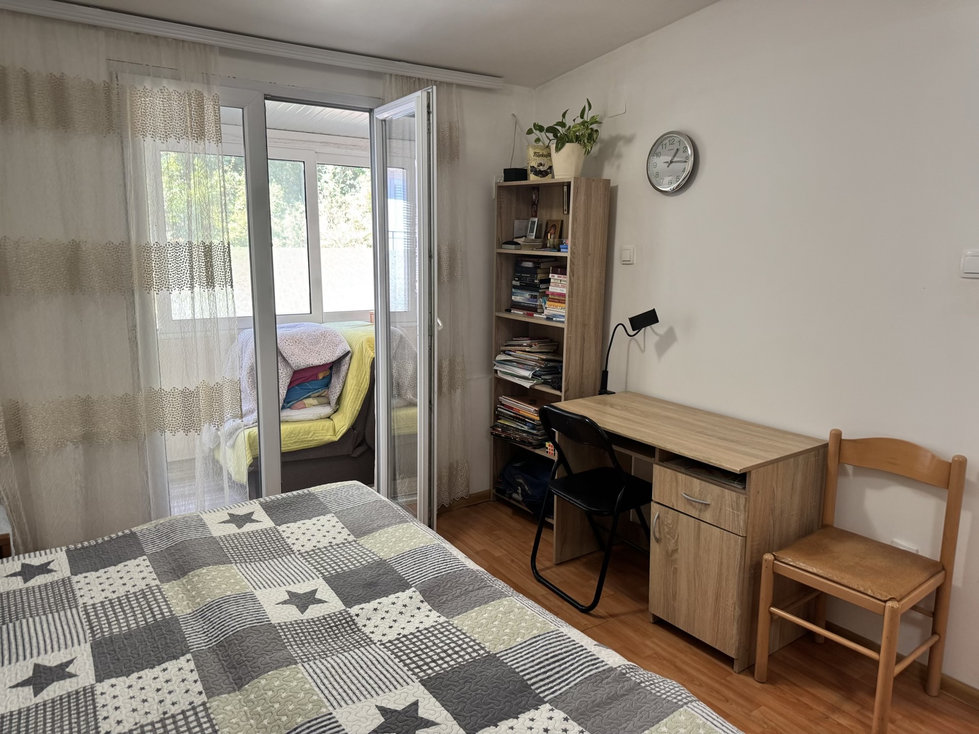 Bedroom in an apartment in Bečići, Montenegro: a bed with a patterned bedspread, a desk, a shelving unit, and access to the balcony.
