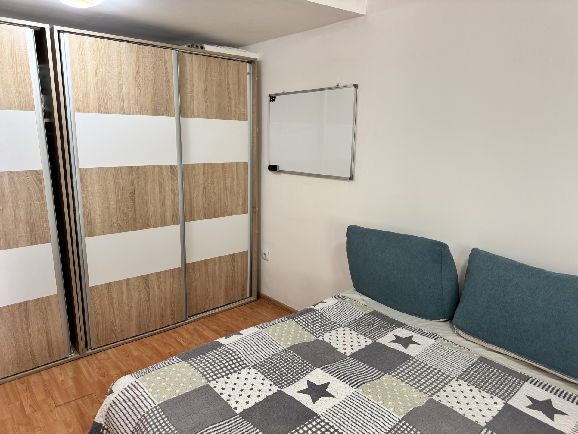 Bedroom in an apartment in Bečići, Montenegro: a double bed, wood-finish sliding wardrobe, and a whiteboard on the wall.