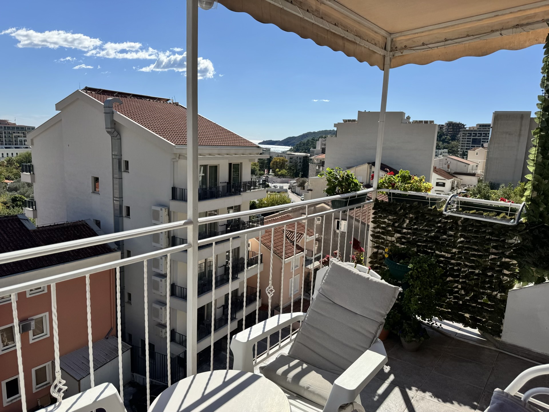 Balcony with furniture and a view of the sea and mountains in an apartment in Becici, Montenegro. Cozy terrace with an awning and greenery.