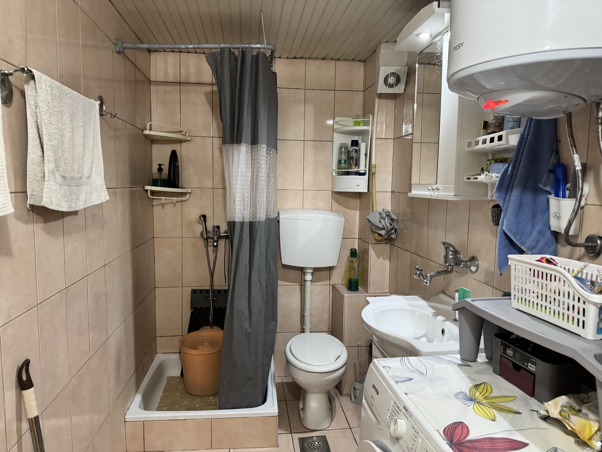 Bathroom in an apartment in Bečići, Montenegro: tiled, shower area with curtain, toilet, and washing machine.