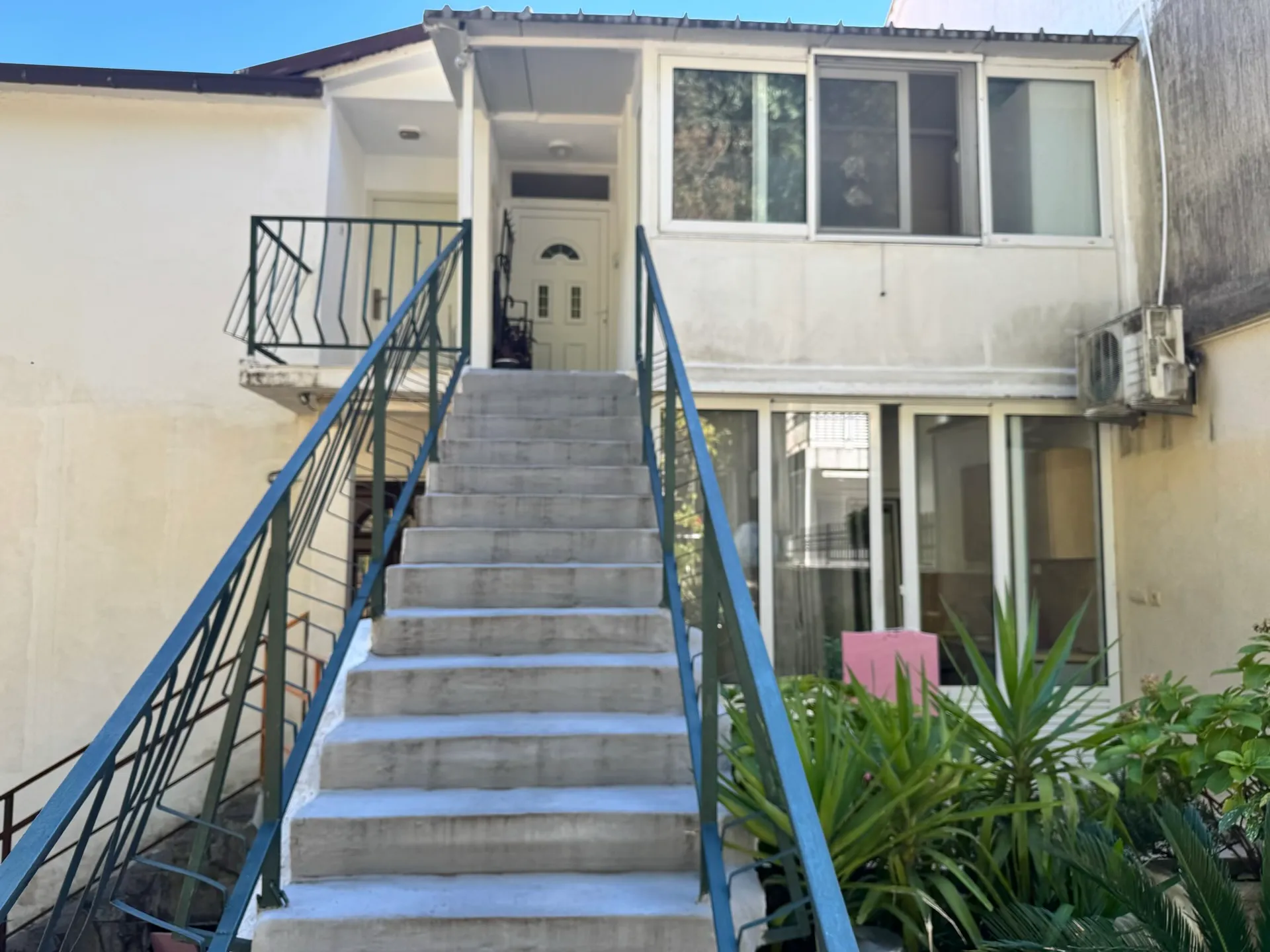 Exterior view of a two-story house with concrete stairs and metal railings leading to the front entrance door.
