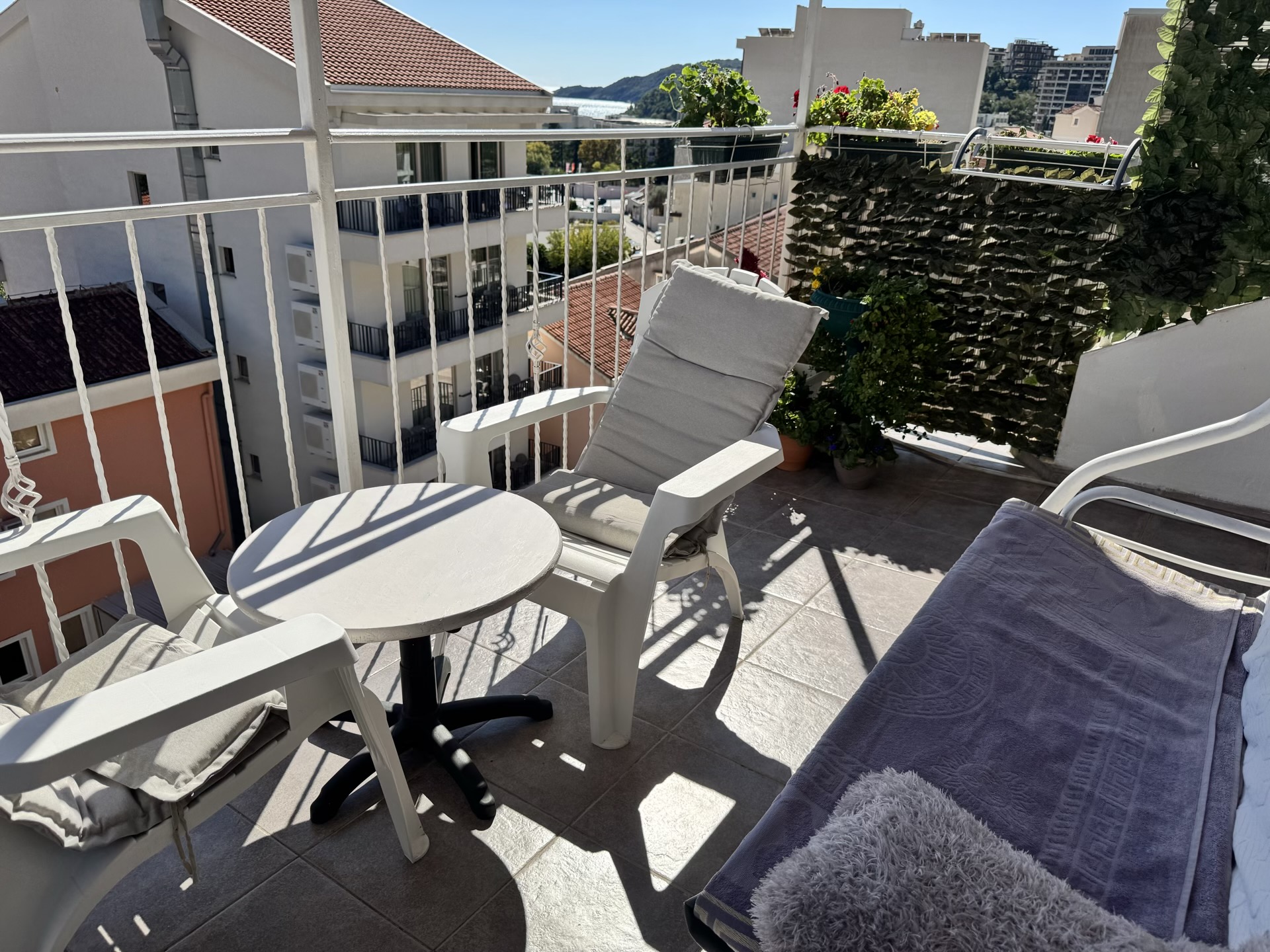 Cozy balcony with furniture and city view in an apartment in Bečići, Montenegro: table, chairs, and live plants.