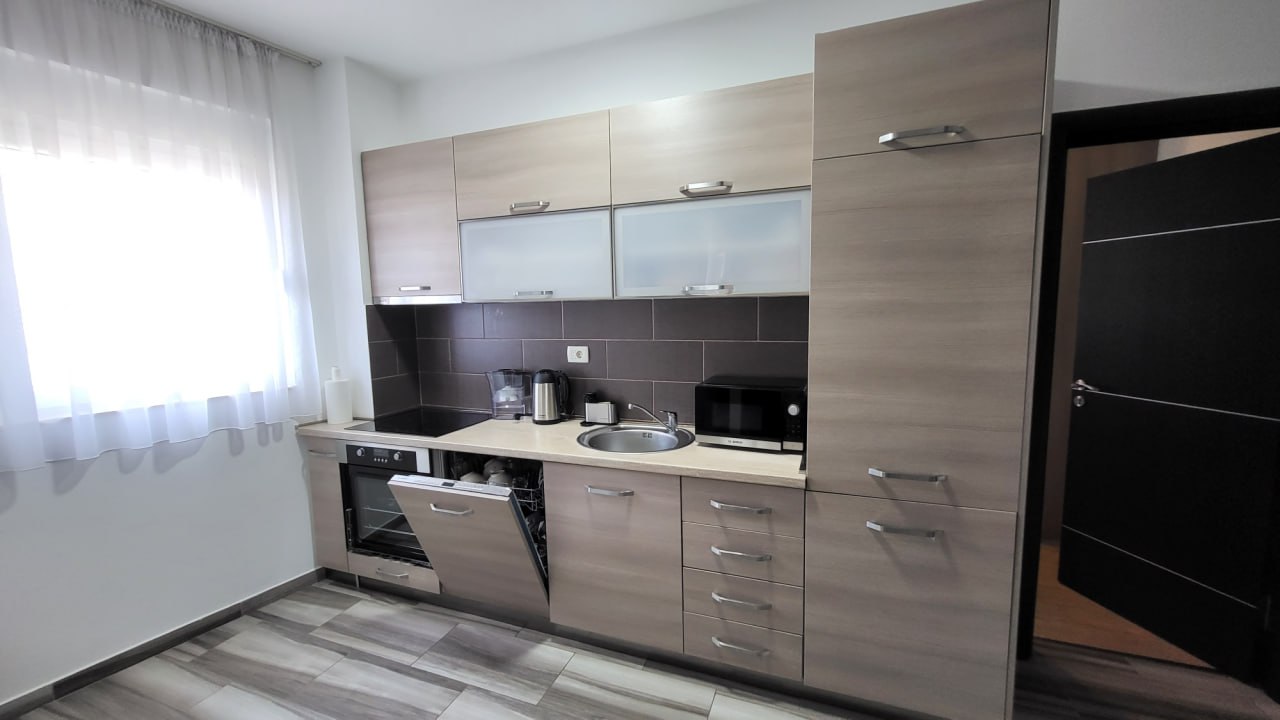 Modern kitchen in an apartment in Bečići, Montenegro: light cabinetry, built-in appliances, and a dark backsplash.