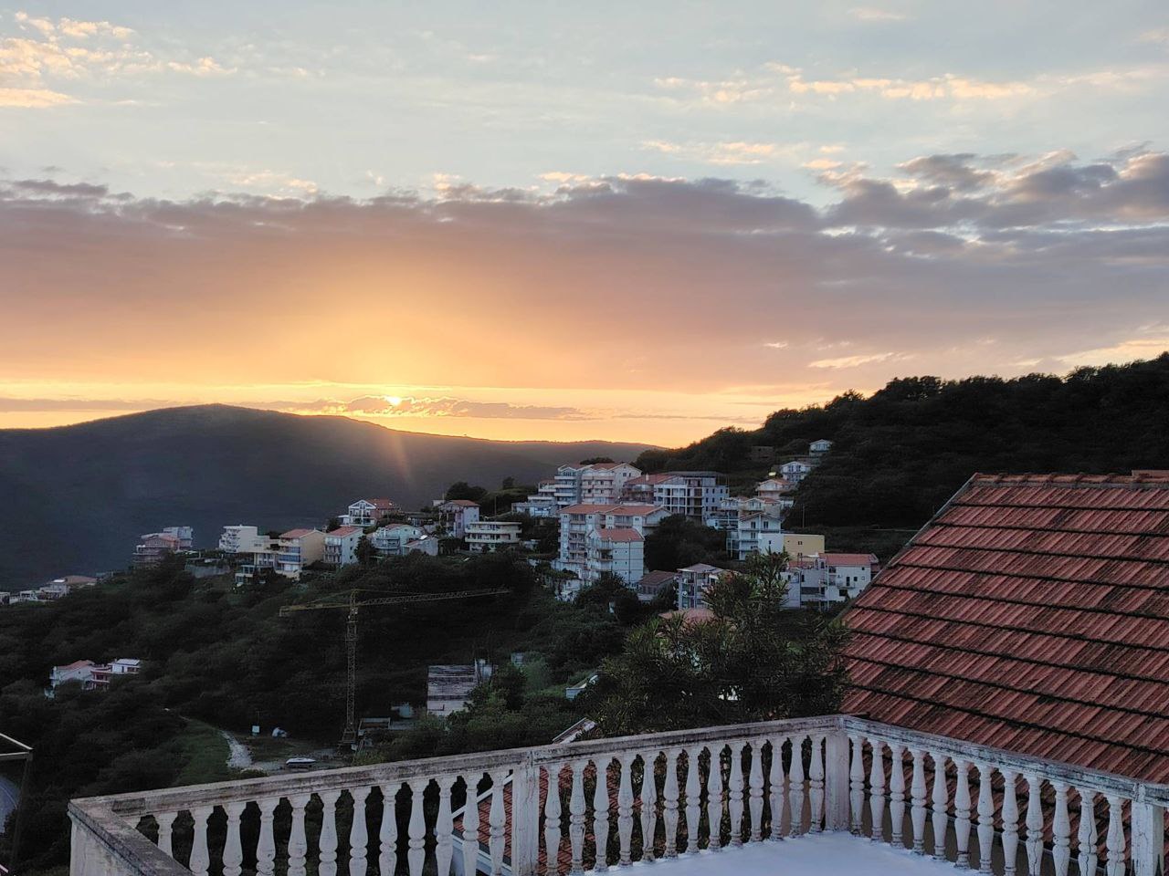 View from the balcony of the sunset and mountains in Seoce, Montenegro: a panorama of the city with tiled roofs and a terrace with a balustrade.