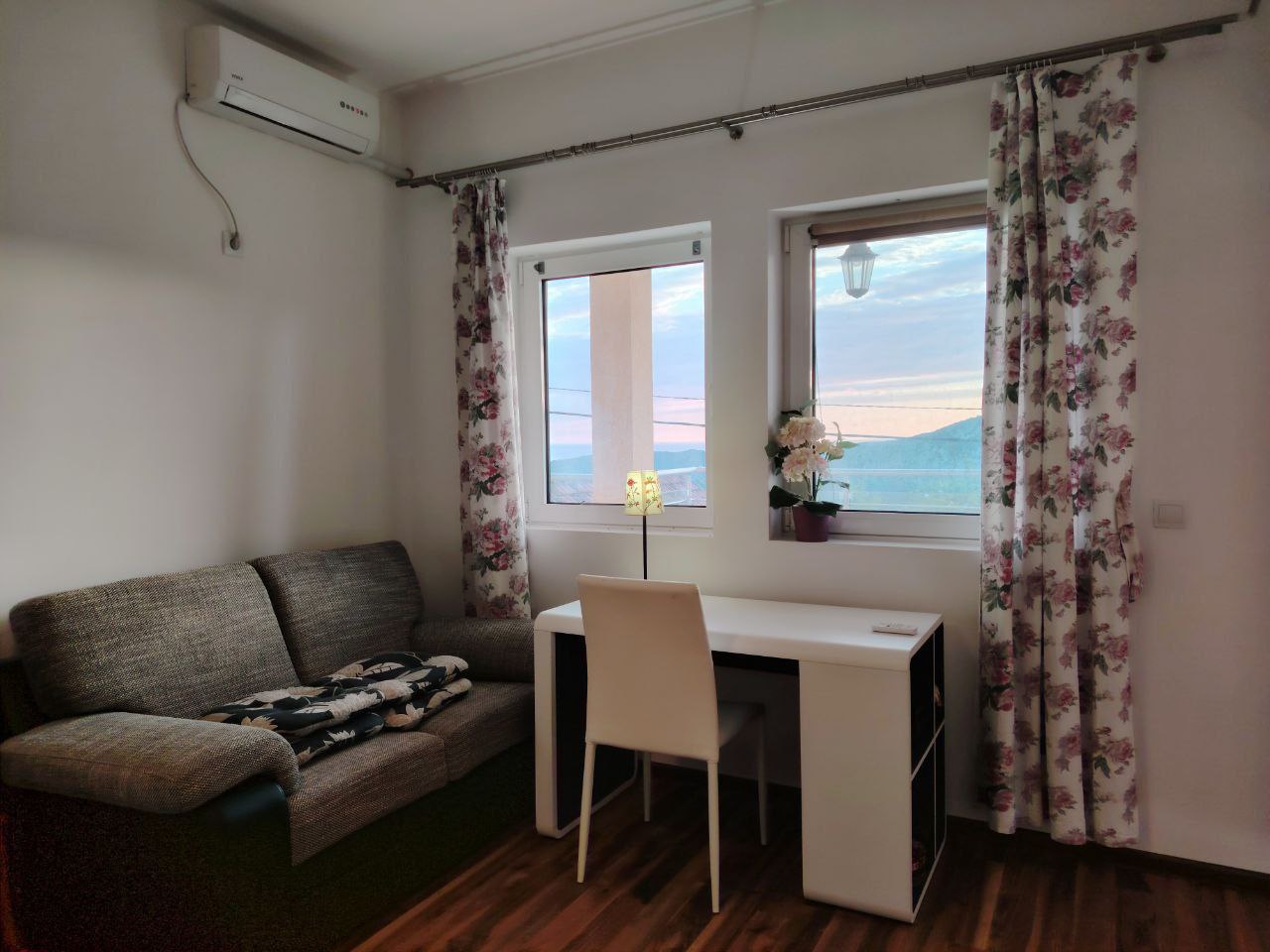 Living room in an apartment in Sutomore, Montenegro: gray sofa, desk, air conditioner, and mountain view from the window.