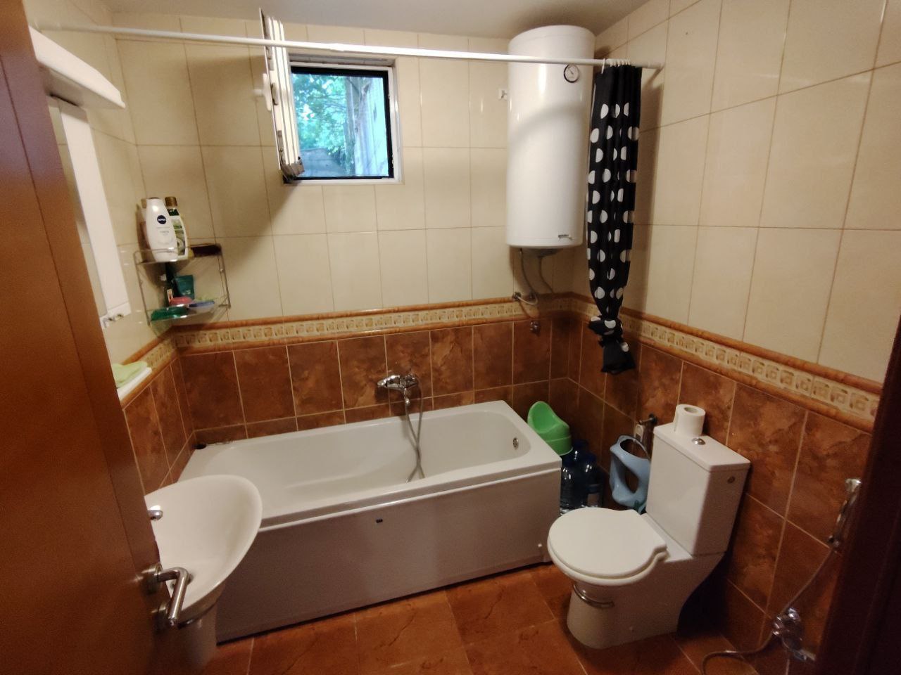 Bathroom in an apartment in Sutomore, Montenegro: tile, bathtub, water heater, toilet, and a window for ventilation.